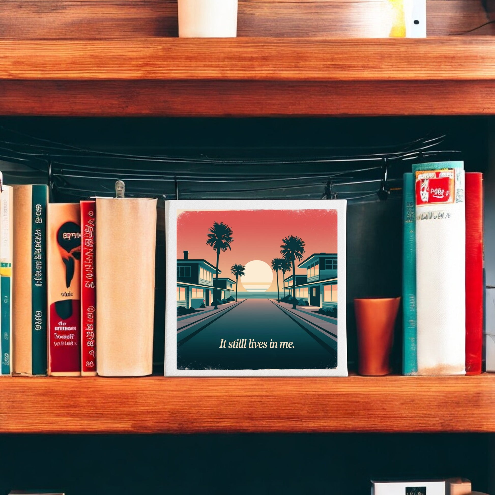 A wooden bookshelf holds several books and a nostalgic "It Still Lives in Me Canvas – Retro Sunset Memory Art" by Mirabilia Boutique, featuring a sunset over a palm-lined street with the text “It still lives in me.”.