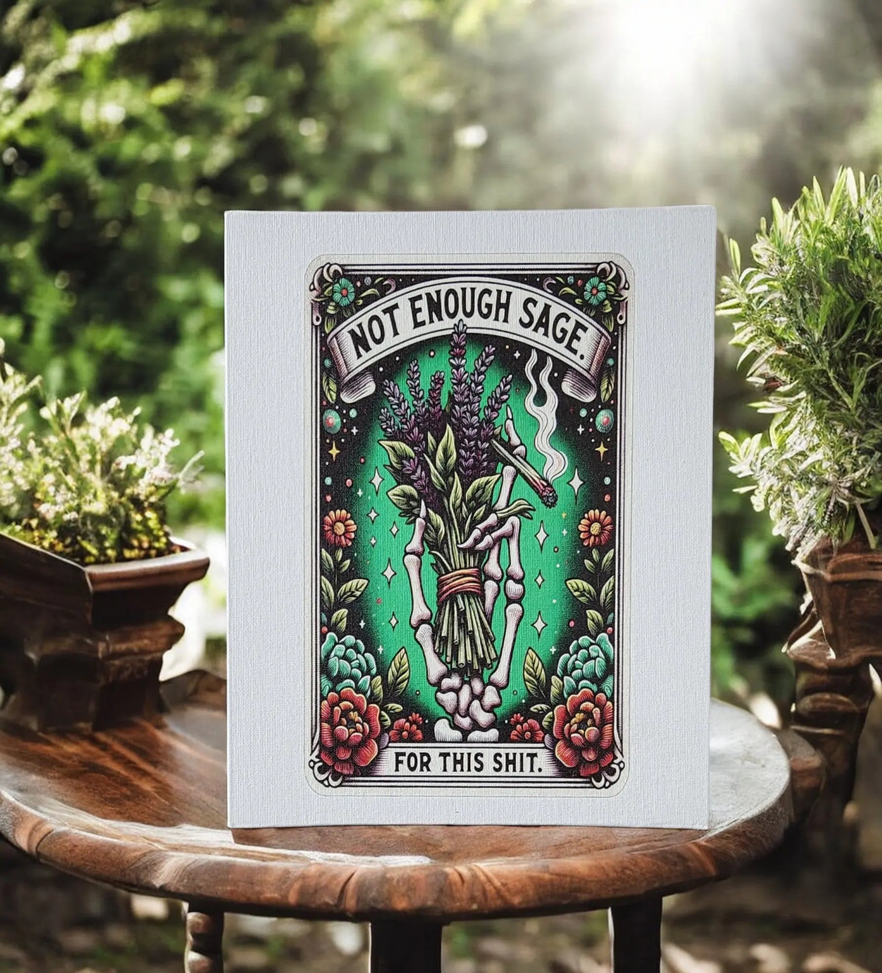 On a wooden table, a humorous card reads "Not enough sage for this shit," making it an ideal gift. The design showcases a bundle of sage, smoke, flowers, and a starry background with surrounding greenery in an outdoor setting—picture it as the Humorous Sage Quote Wall Art Print by Mirabilia Boutique to capture the vibe indoors for home or office decor.