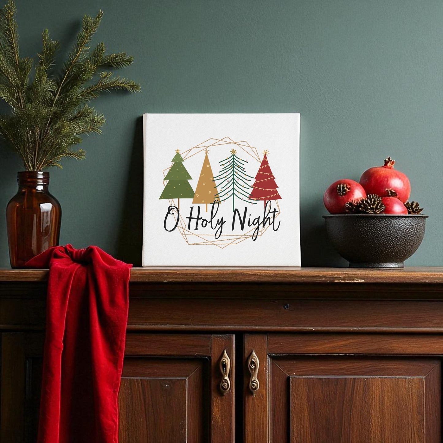 A festive wooden sideboard displays pine branches, pomegranates, a red cloth, and the Mirabilia Boutique “O Holy Night Canvas Sign | Christmas Wall Decor 8x8,” a minimalist faith-inspired sign with decorated trees.
