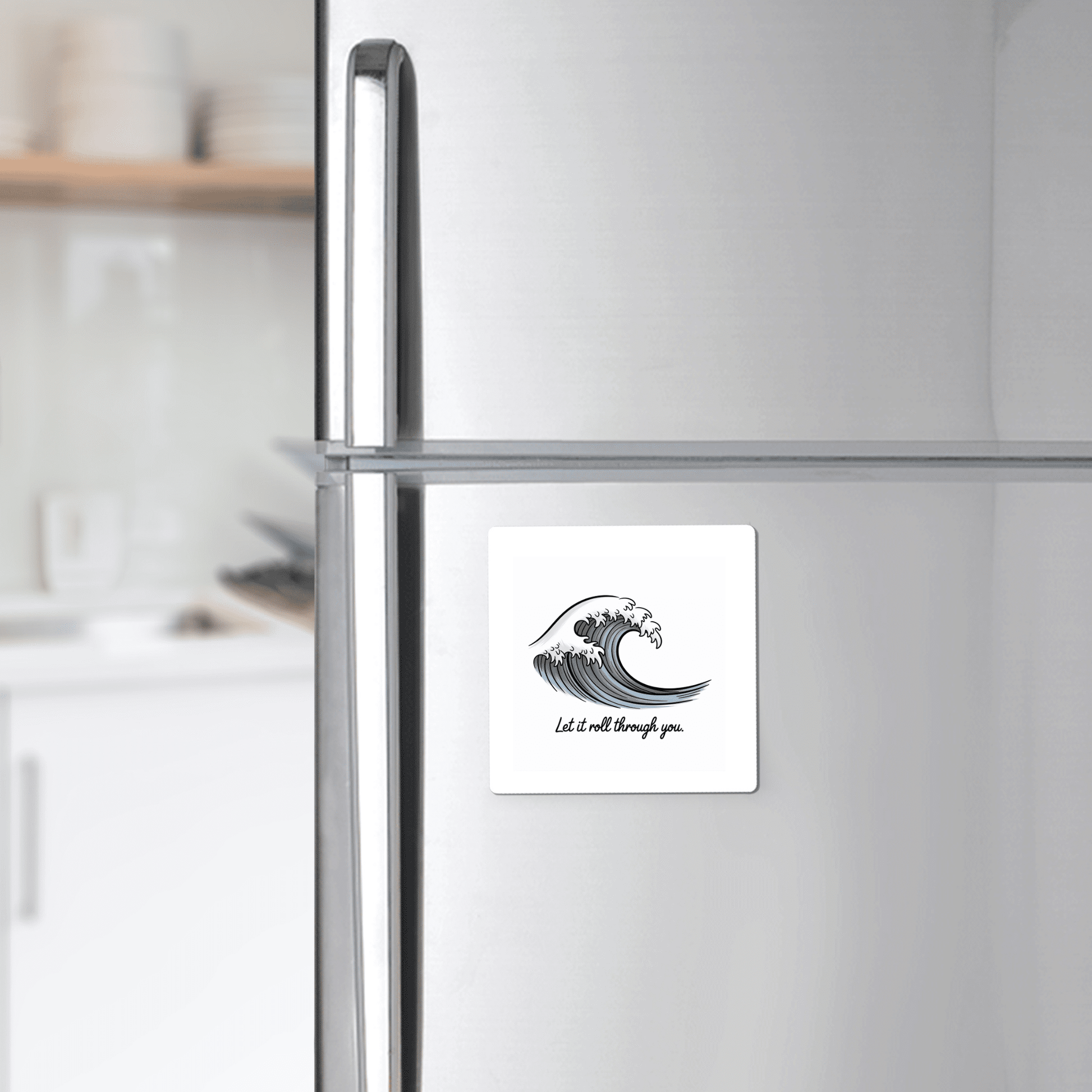 A stainless steel fridge displays the Mirabilia Boutique "Let It Roll Through You Magnet – Ocean-Inspired Calm," featuring a square blue wave design and uplifting text. A modern kitchen is shown in the background.