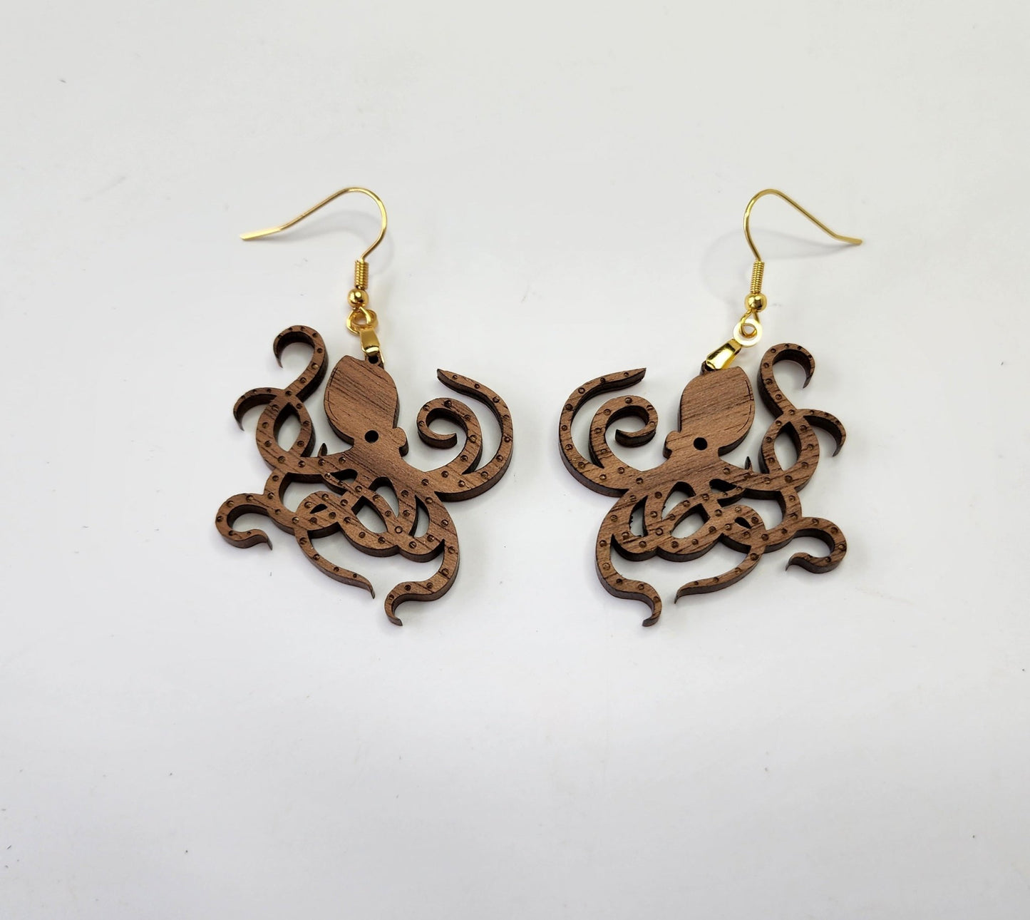 Displayed against a plain white background, the Octopus Earrings by Mirabilia Boutique feature laser-cut walnut wood octopus shapes and gold hooks.