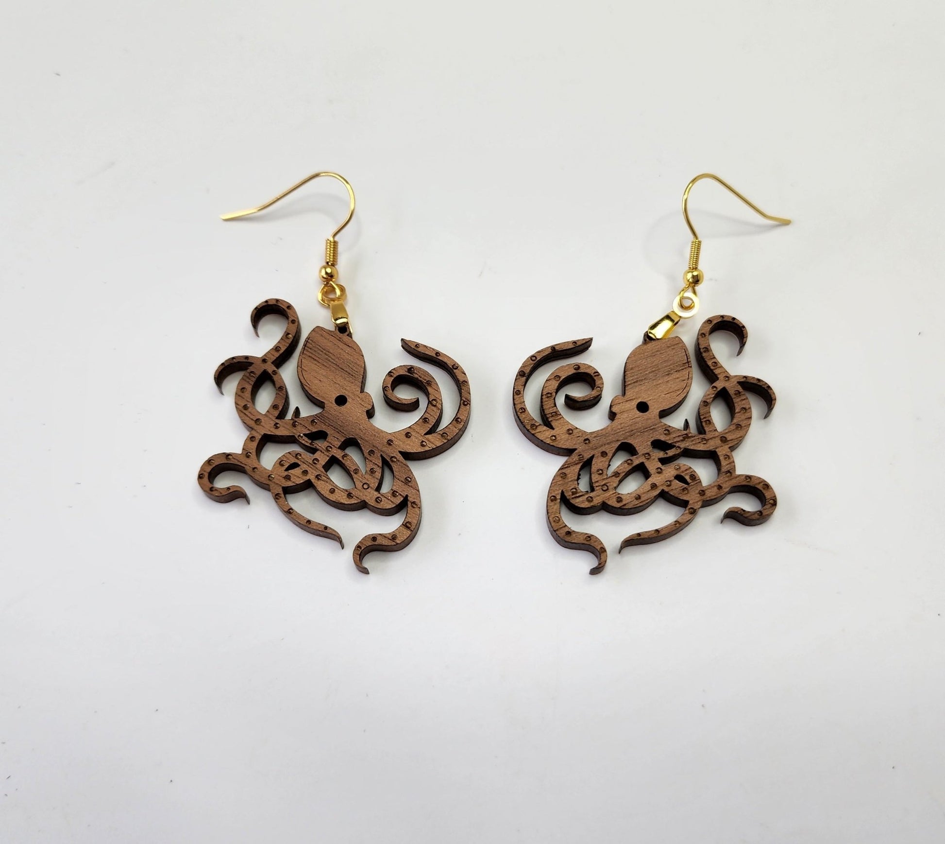 Displayed against a plain white background, the Octopus Earrings by Mirabilia Boutique feature laser-cut walnut wood octopus shapes and gold hooks.