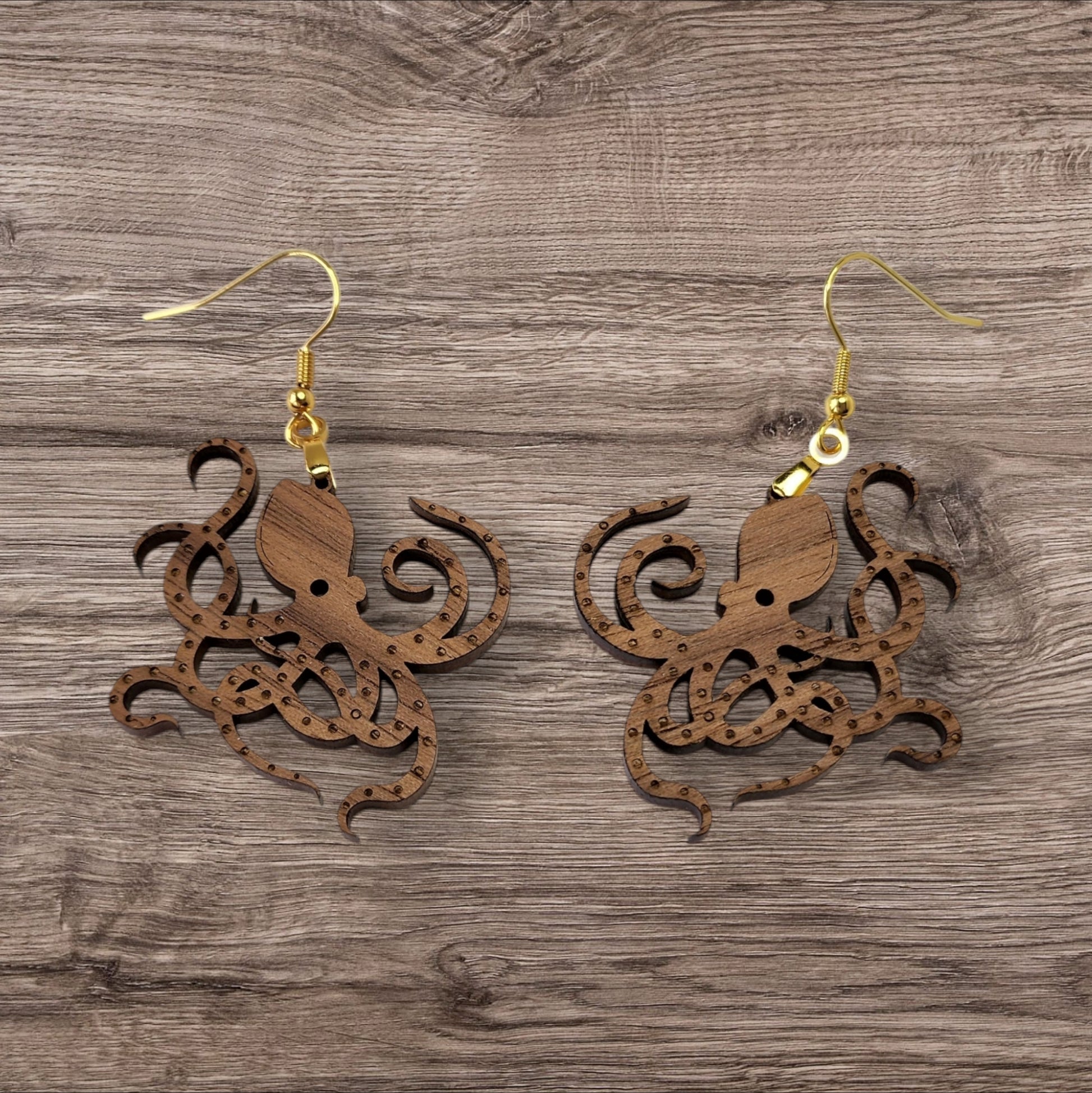 Mirabilia Boutique presents the Octopus Earrings: intricately laser-cut, walnut wood earrings featuring detailed tentacles and gold hooks, elegantly set on a textured wooden surface.