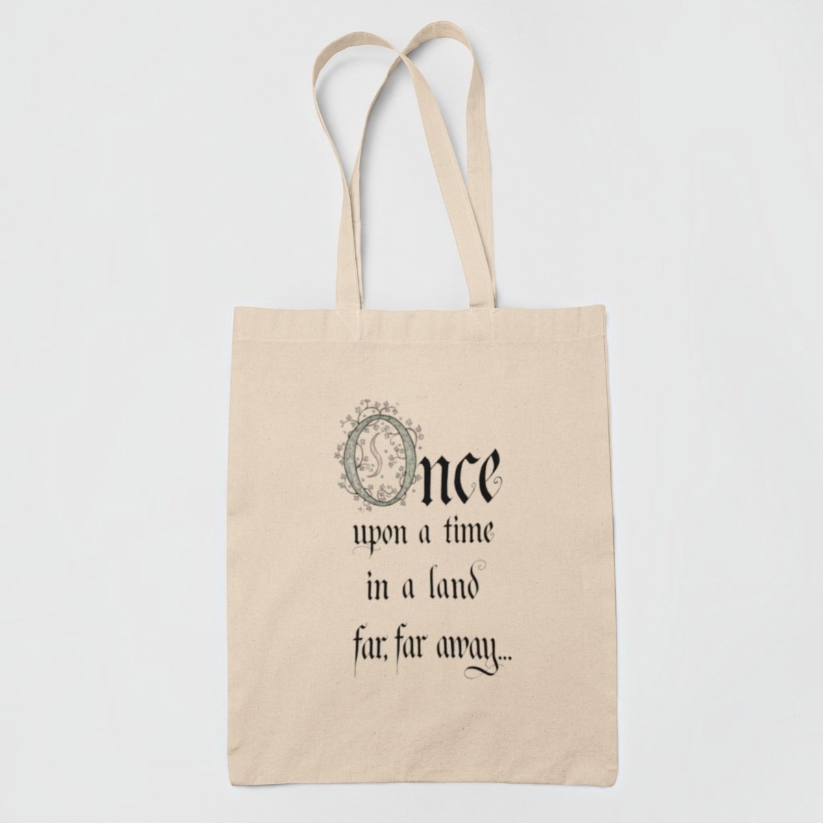 Introducing the "Once Upon a Time Fairytale Tote Bag" from Mirabilia Boutique—a beige tote adorned with the phrase "Once upon a time in a land far, far away..." elegantly scripted in decorative black font. The ornate “O” features an exquisite floral motif, making this enchanting bag an ideal accessory for literary enthusiasts and fairytale fans alike.