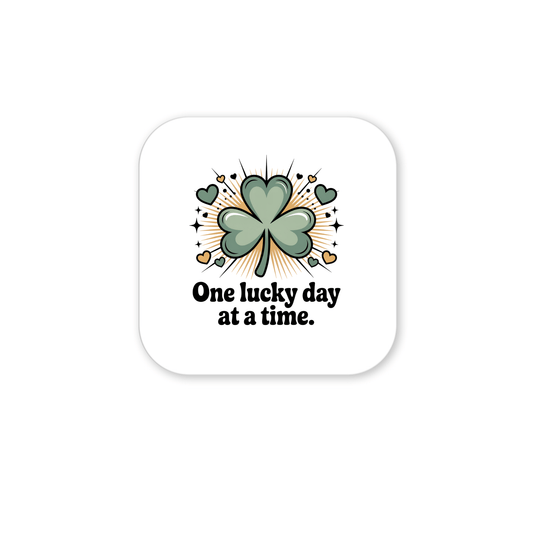 The One Lucky Day at a Time Magnet by Mirabilia Boutique features a green four-leaf clover with hearts and sparkles, and the phrase "One lucky day at a time" on a white rounded square—ideal for St. Patrick’s Day charm.
