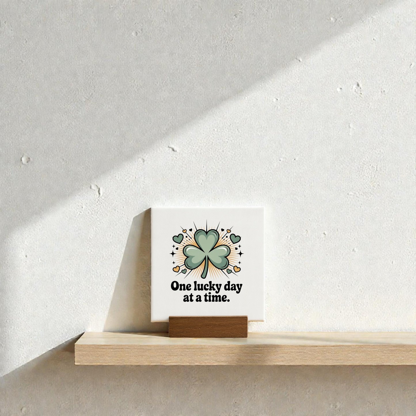 The One Lucky Day at a Time Mini Sign – 4x4 by Mirabilia Boutique features a green four-leaf clover and sits on a wooden stand, making a charming gift for good fortune and encouragement.