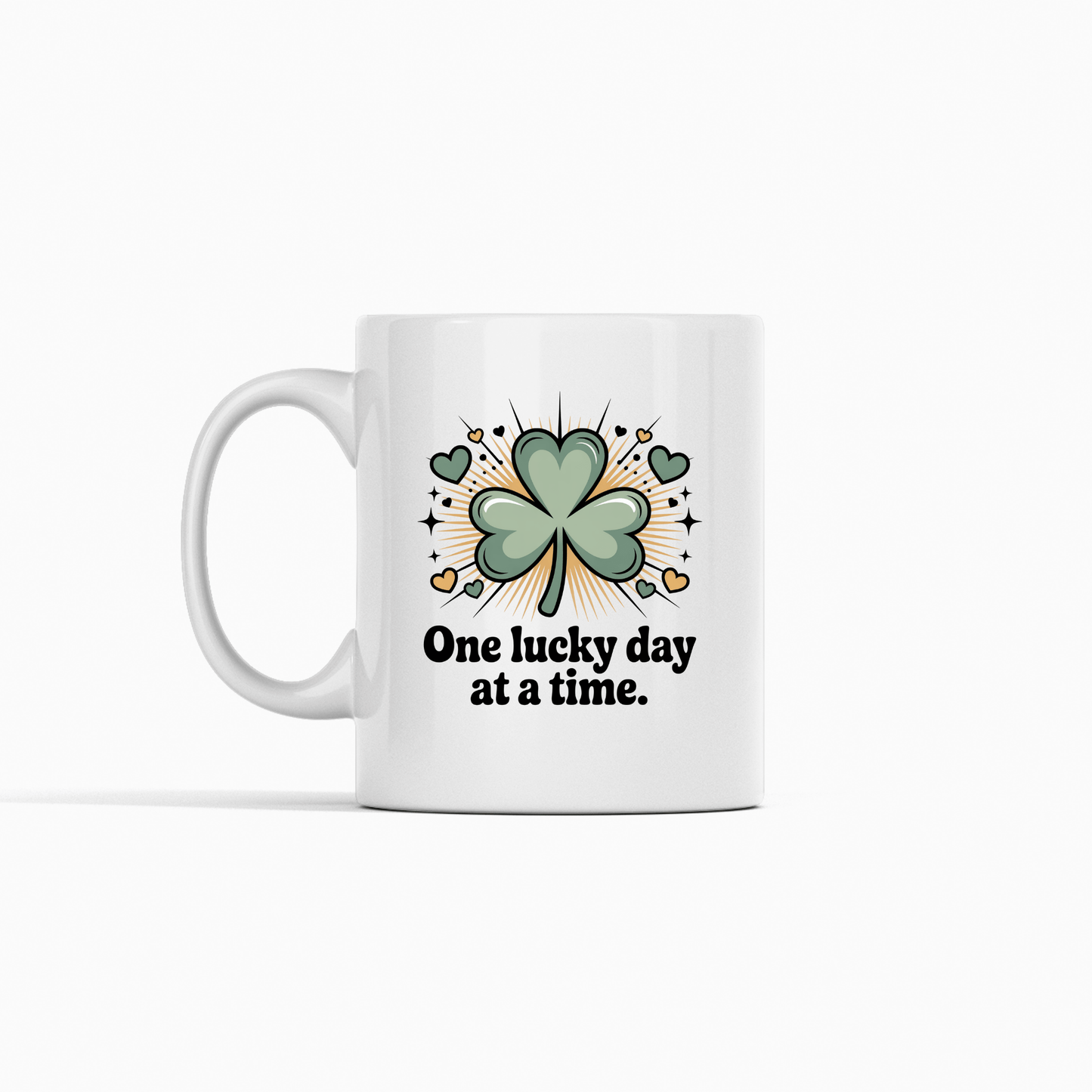 Enjoy your daily coffee with the Mirabilia Boutique 'One Lucky Day at a Time Mug'—a ceramic cup featuring a green shamrock with hearts, sparkles, and an inspiring phrase. Perfect for bringing good fortune to every sip!.