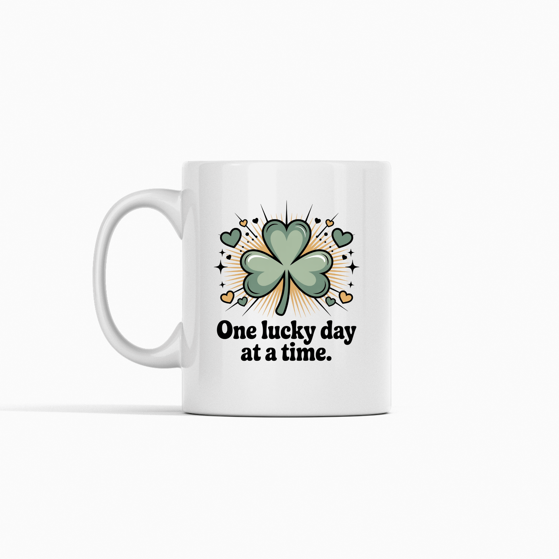 Enjoy your daily coffee with the Mirabilia Boutique 'One Lucky Day at a Time Mug'—a ceramic cup featuring a green shamrock with hearts, sparkles, and an inspiring phrase. Perfect for bringing good fortune to every sip!.