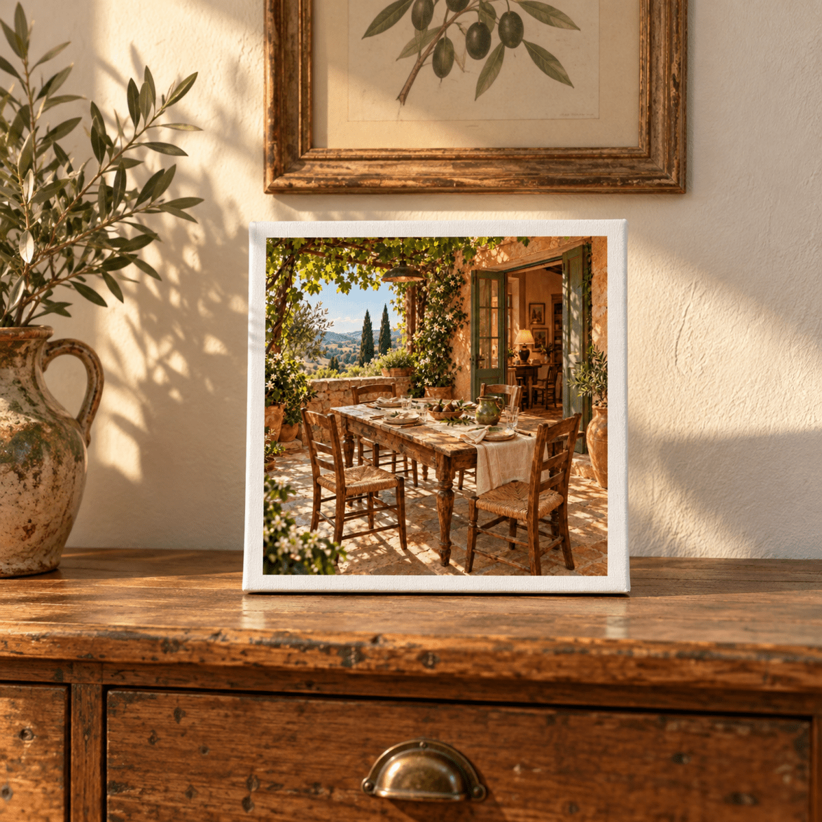 One More Place Tuscan Canvas Art | Ochre & Cypress displayed on a wooden dresser, featuring a sunlit stone patio with an outdoor dining table in the style of a Tuscan country house.