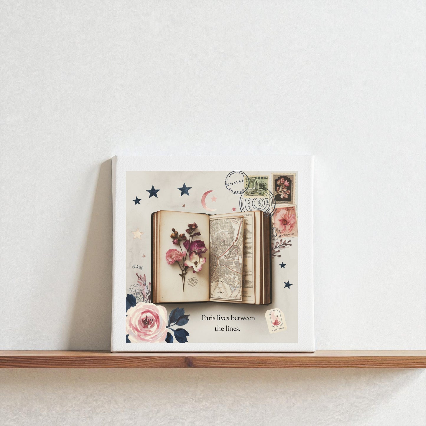 The Paris Between the Lines Canvas – Literary Floral 8x8 Art by Mirabilia Boutique features flowers, a book, a map, stamps, and stars with the caption "Paris lives between the lines"—ideal wall art for literary or Paris lovers.