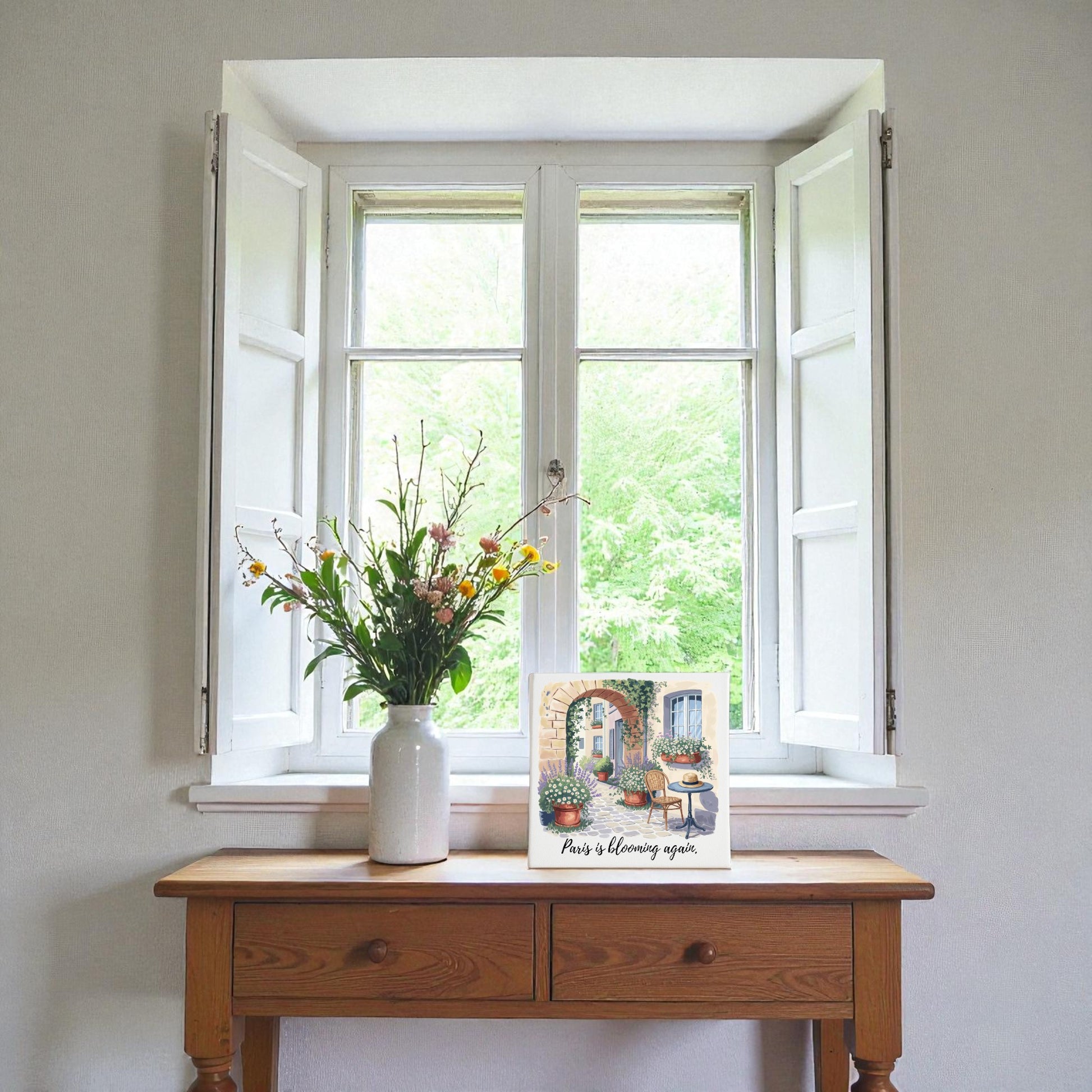 The Mirabilia Boutique "Paris Is Blooming Again" Canvas Wall Art rests on a wooden table by a sunlit window, capturing the fresh, inviting feel of French springtime decor.