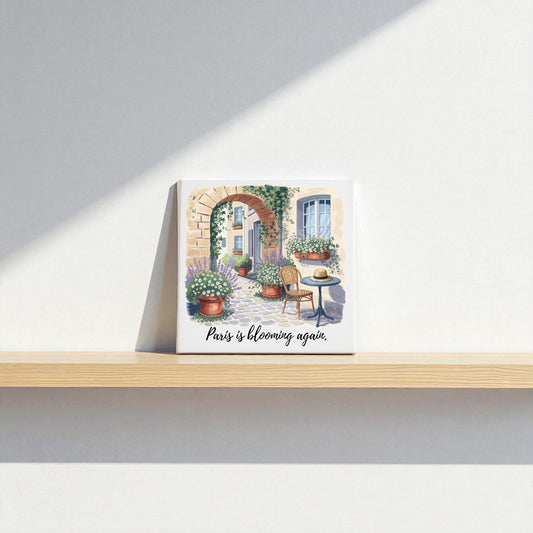 A square Paris Is Blooming Again Canvas Wall Art by Mirabilia Boutique sits on a wooden shelf against a white wall, showcasing flowers, pots, and a chair—romantic French springtime decor for your home.