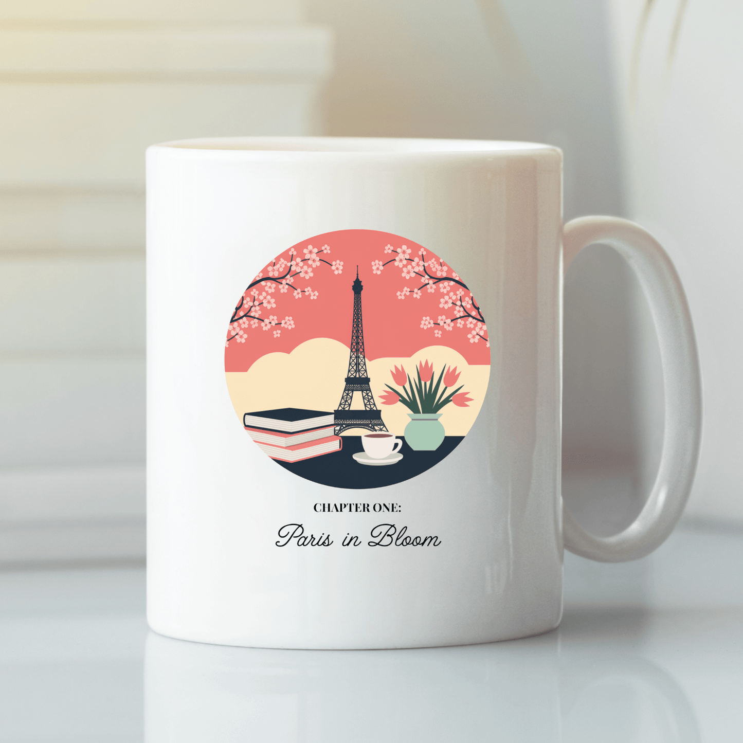 The Paris Book Lover Mug – Chapter One: Paris in Bloom by Mirabilia Boutique features the Eiffel Tower, books, a teacup, and cherry blossoms—an ideal gift for book lovers. Text: “Chapter One: Paris in Bloom.”.
