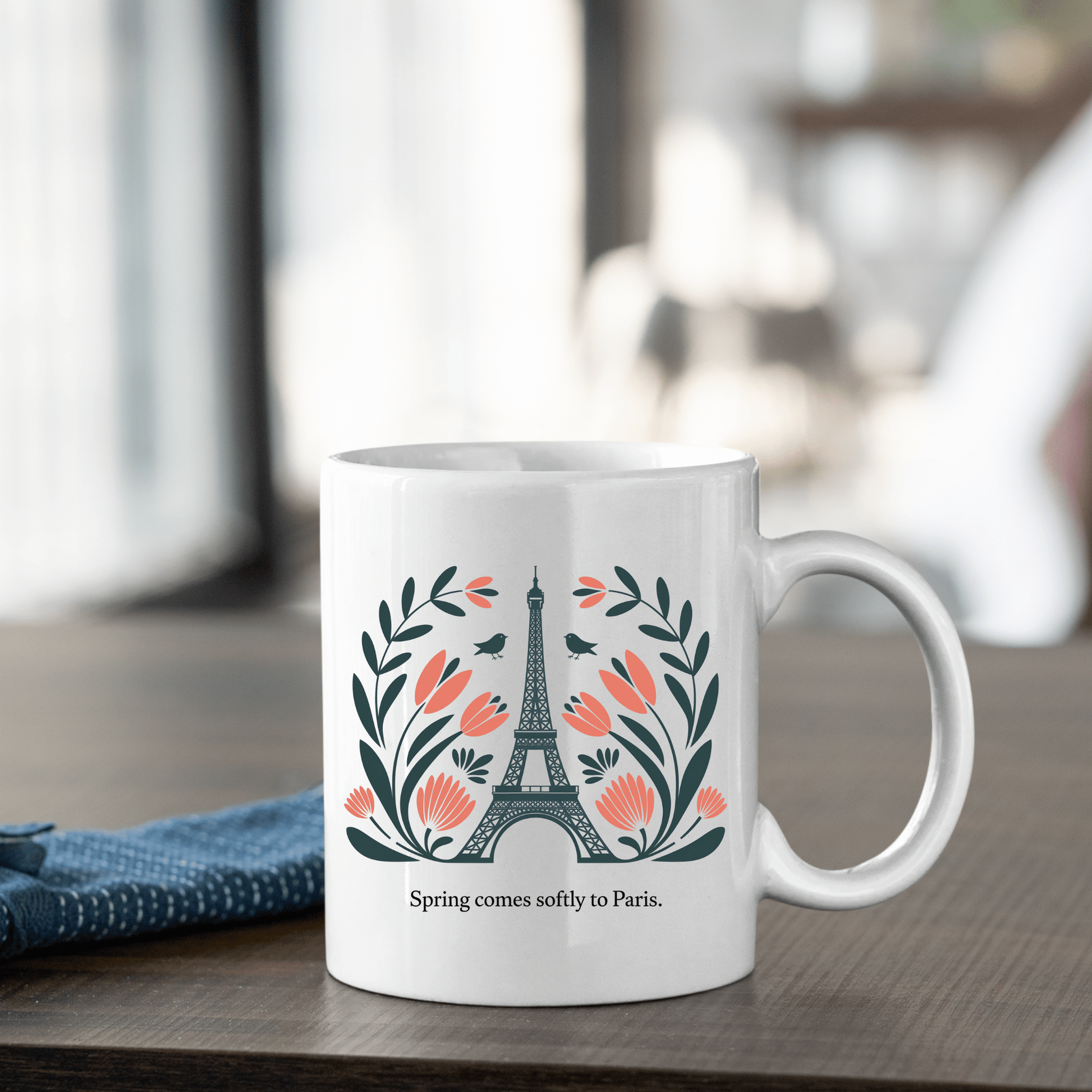 The Paris Spring Mug – Eiffel Tower & Floral Design by Mirabilia Boutique features an illustration of the Eiffel Tower with pink flowers and green leaves, plus "Spring comes softly to Paris." printed below—all on a charming ceramic mug.