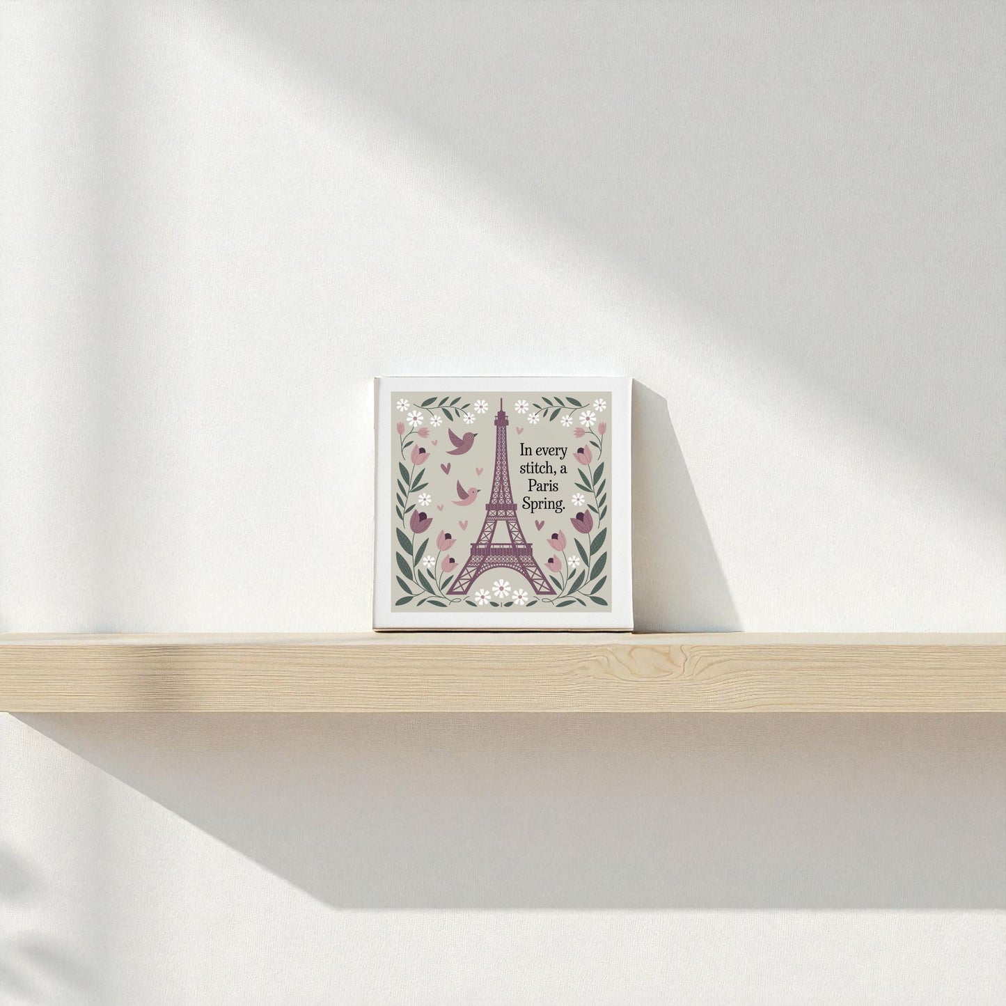 The Paris Spring Stitch Canvas by Mirabilia Boutique, an embroidered-style floral artwork with birds and the quote "In every ditch, a Florida Spring," sits on a light wooden shelf against a white wall with soft shadows.