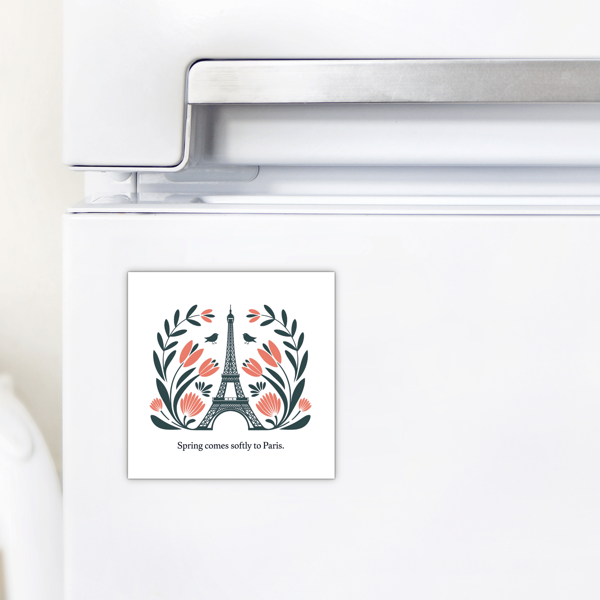 The Mirabilia Boutique Spring Comes Softly to Paris – Floral Eiffel Magnet features the Eiffel Tower with leaves and pink flowers, plus the text "Spring comes softly to Paris." Perfect for your refrigerator!.