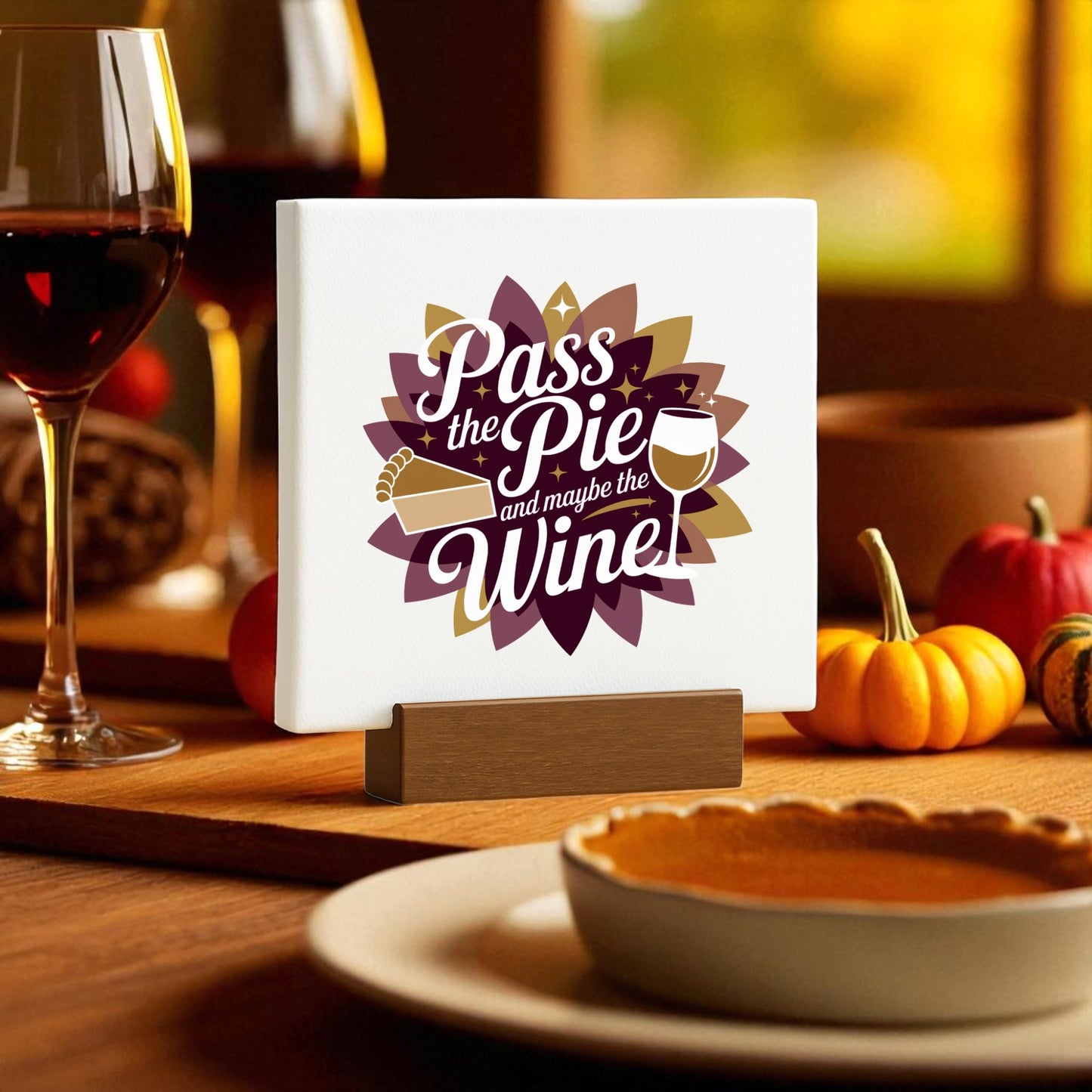 A festive table with fall decor, wine glasses, small pumpkins, and the Mirabilia Boutique "Pass the Pie and Maybe the Wine Mini Fall Sign"—a Thanksgiving accent featuring cozy pie and wine glass graphics in warm autumn light.