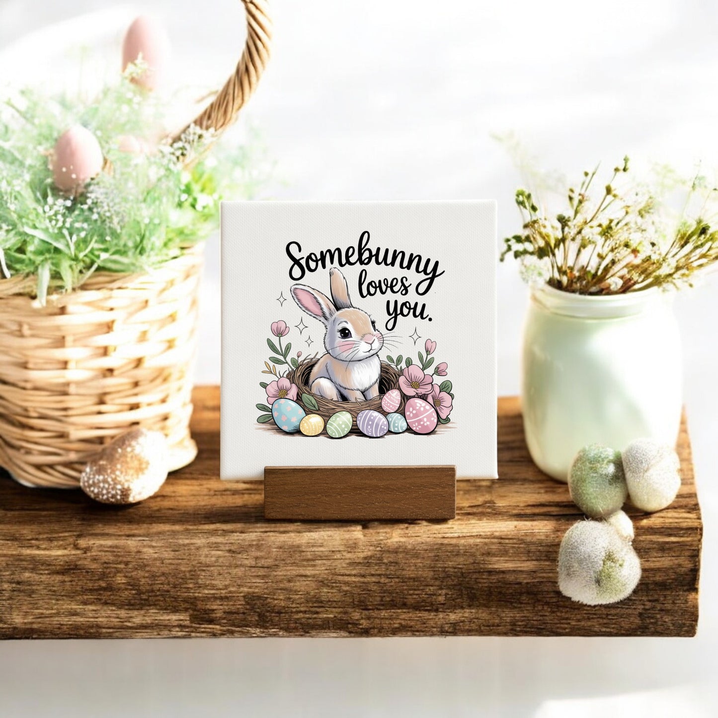 The Mirabilia Boutique "Somebunny Loves You" Mini Canvas (4x4) with wood stand features a bunny, pastel eggs, and flowers—perfect for spring decor or as an Easter basket filler.