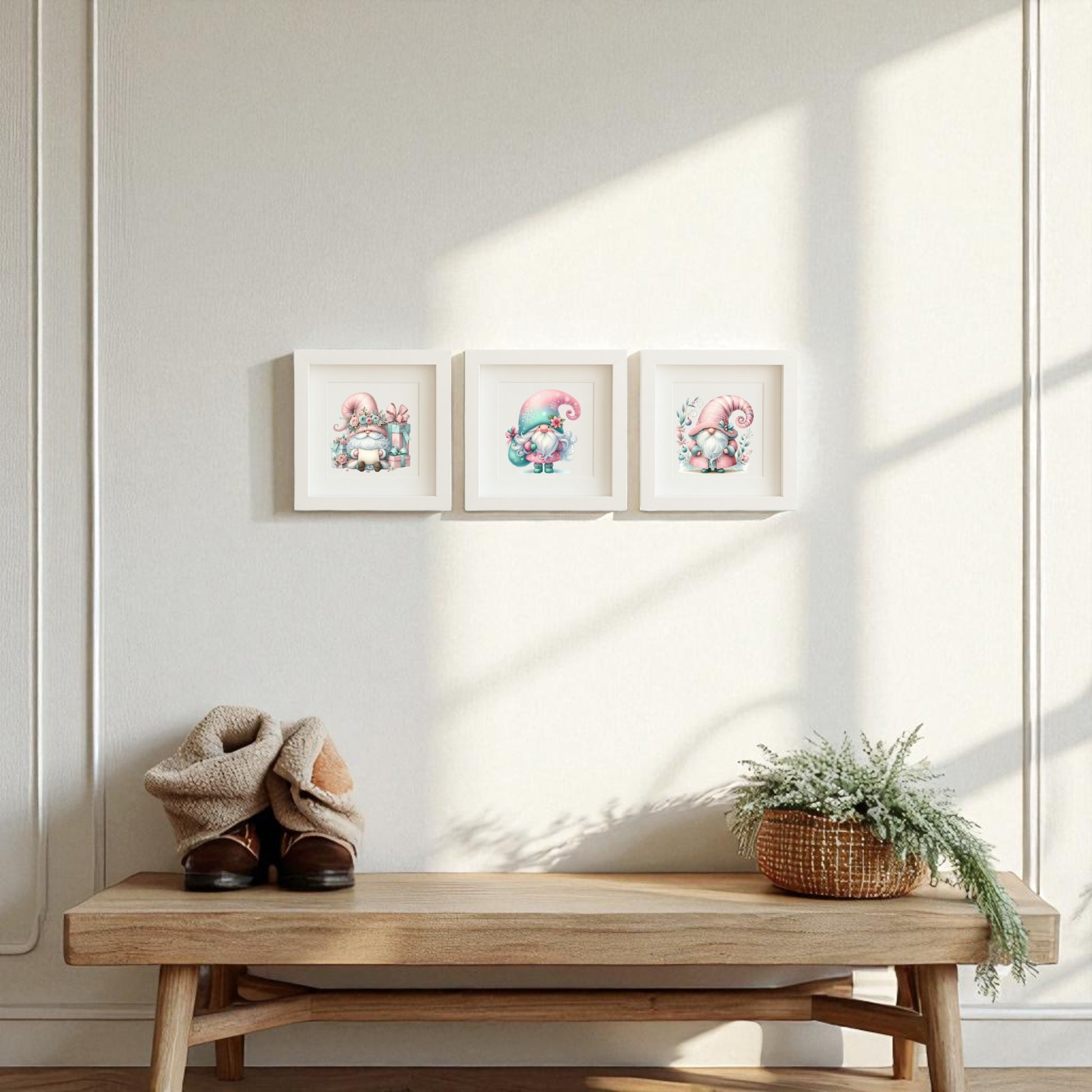 A wooden bench with blankets, boots, and a greenery-filled basket sits against a light wall, above which hangs the Pastel Gnome Wall Art Trio by Mirabilia Boutique—three whimsical winter prints in a row. Sunlight casts gentle shadows nearby.