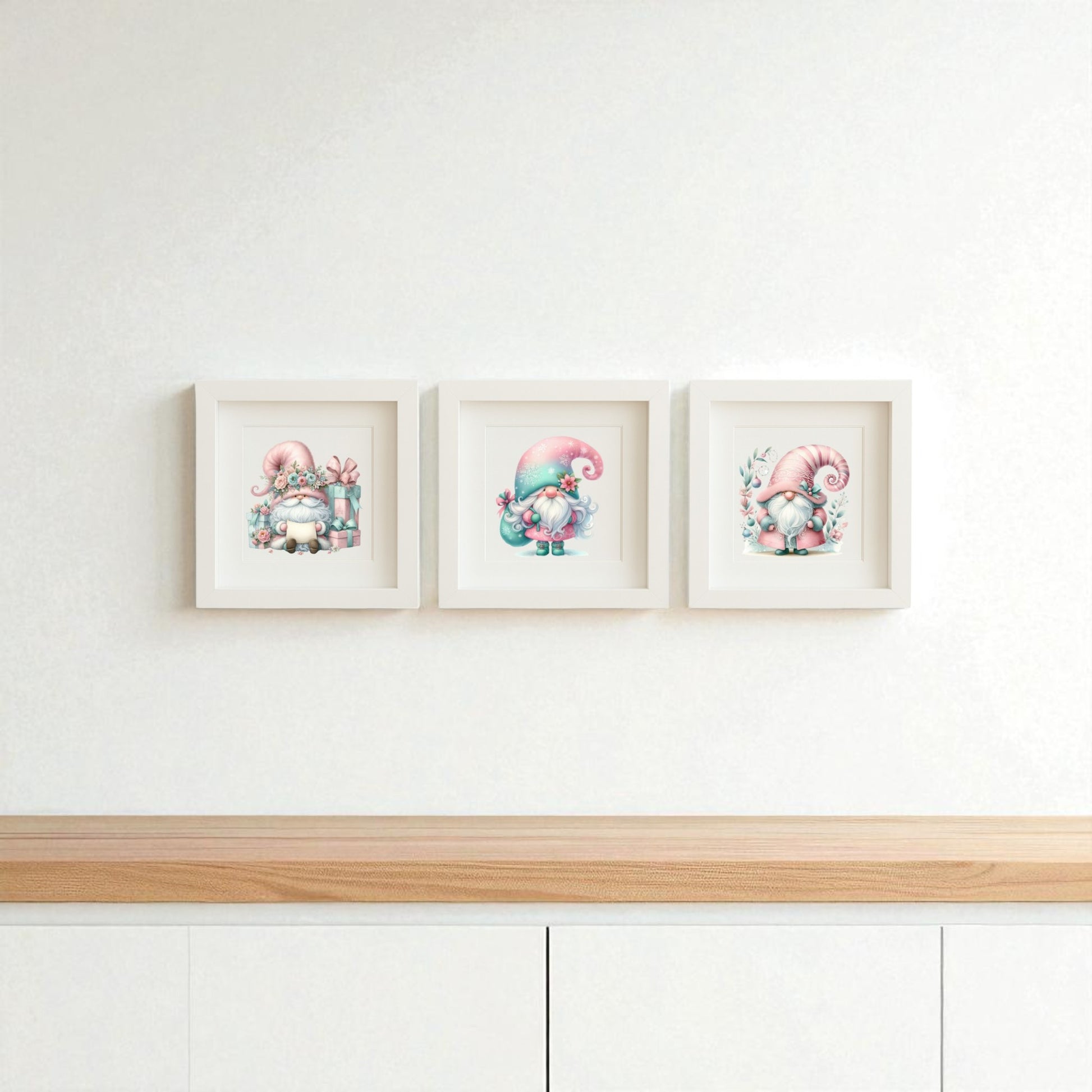 The Pastel Gnome Wall Art Trio by Mirabilia Boutique features three framed prints with pink-hatted gnomes on a clean white wall above a light wood cabinet—perfect for whimsical nursery or winter holiday decor.