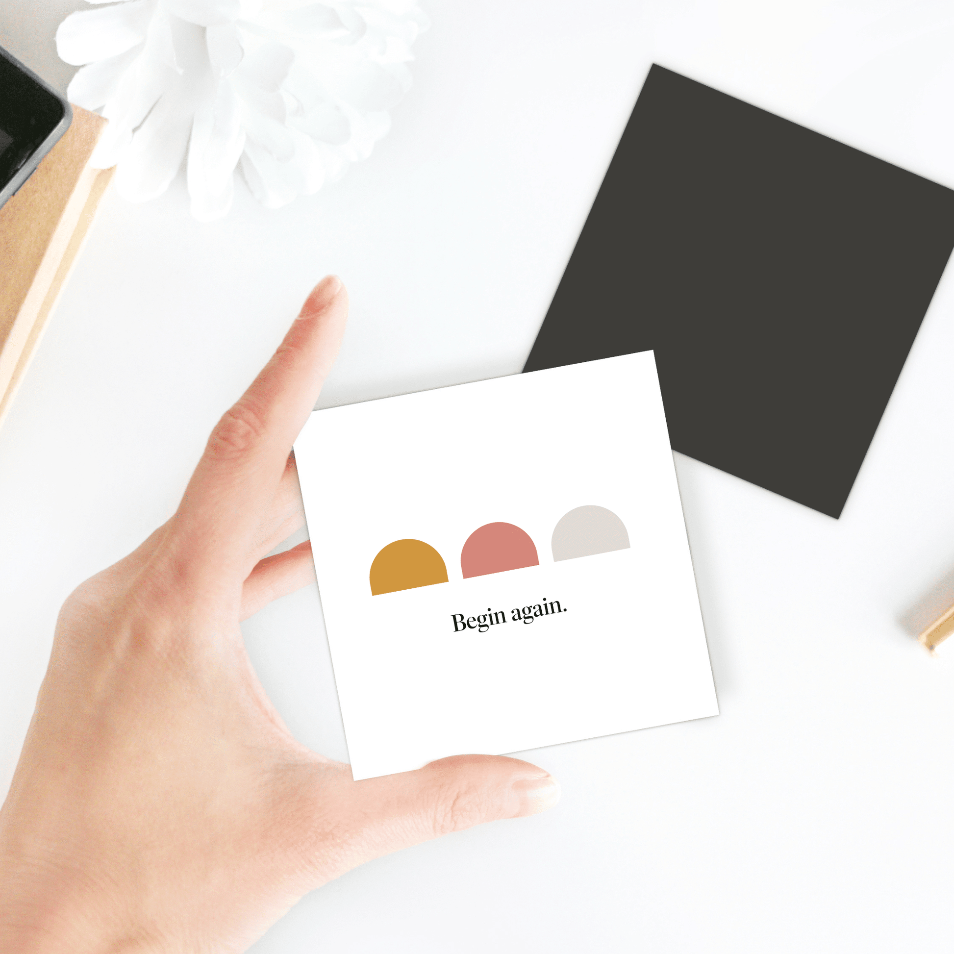 A hand holds the Begin Again Magnet – Minimalist Summer Affirmation by Mirabilia Boutique, featuring three colored semi-circles and the words "Begin again." Perfect as an inspiring fridge magnet for your space.
