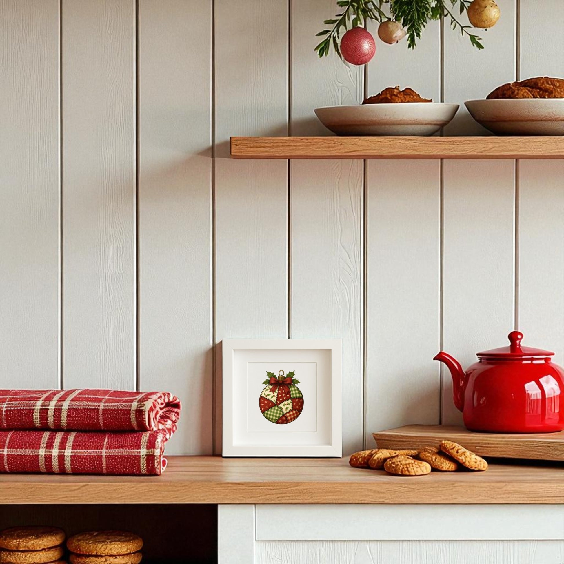 A cozy kitchen with red accents—like a teapot, plaid towels, and cookies—features open shelves of dishes and baked goods. A Mirabilia Boutique Patchwork Ornament Sign (5x5 Christmas Shadowbox Wall Art) decorates the white paneled wall.