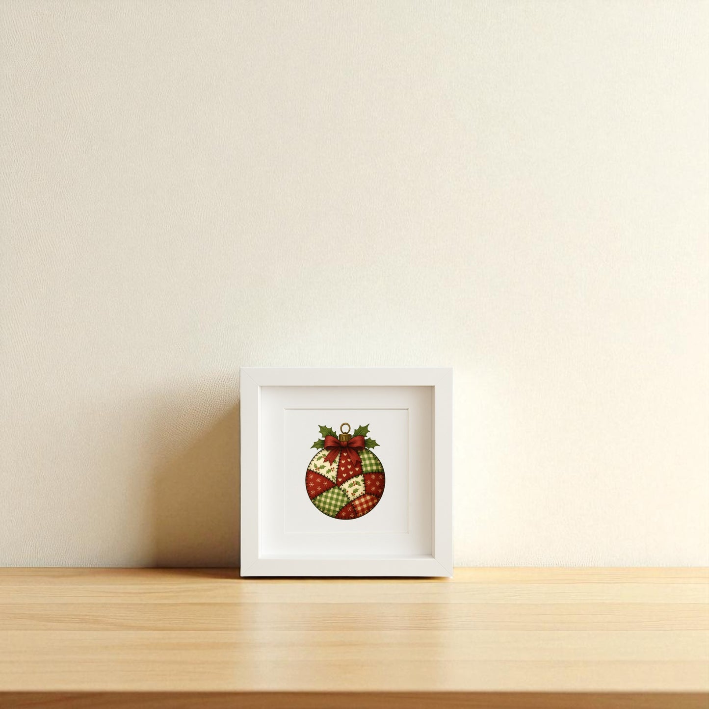 The Patchwork Ornament Sign | 5x5 Christmas Shadowbox Wall Art by Mirabilia Boutique features a red and green ornament with holly leaves and berries, displayed in a frame on a light wooden surface against a beige wall. Perfect for cozy farmhouse décor.