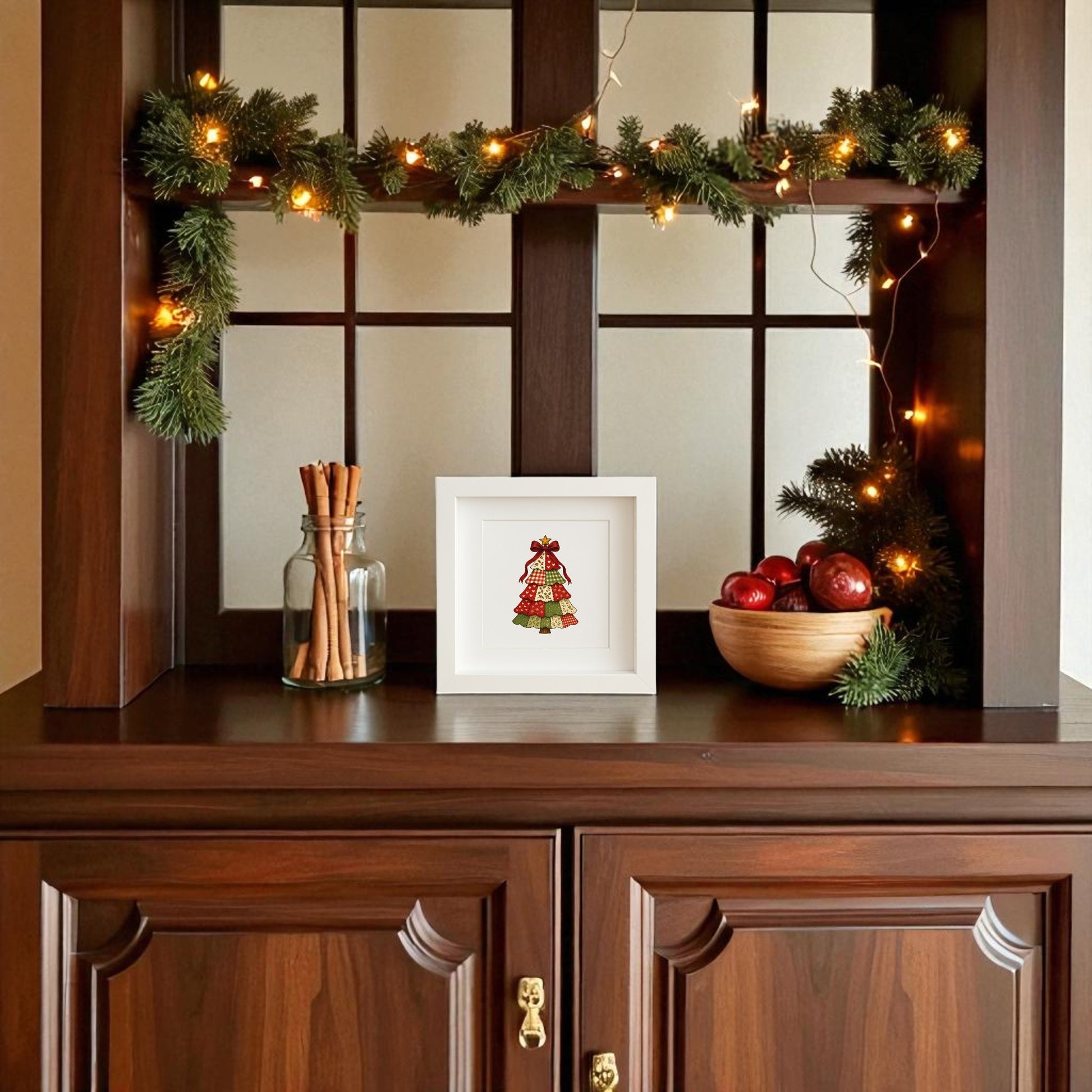 A wooden cabinet with a pine garland and string lights displays jars of cinnamon sticks, a bowl of red apples with pine, and the Mirabilia Boutique Patchwork Christmas Tree Sign (5x5 Shadowbox Holiday Decor) on the shelf.
