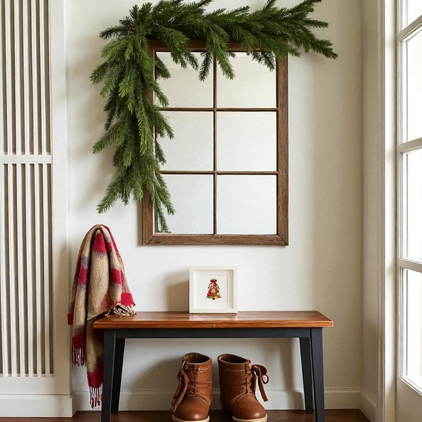 A wooden bench with brown boots, a red plaid scarf, and the Patchwork Christmas Tree Sign by Mirabilia Boutique sits beneath a mirror decorated with pine garland in a bright entryway.