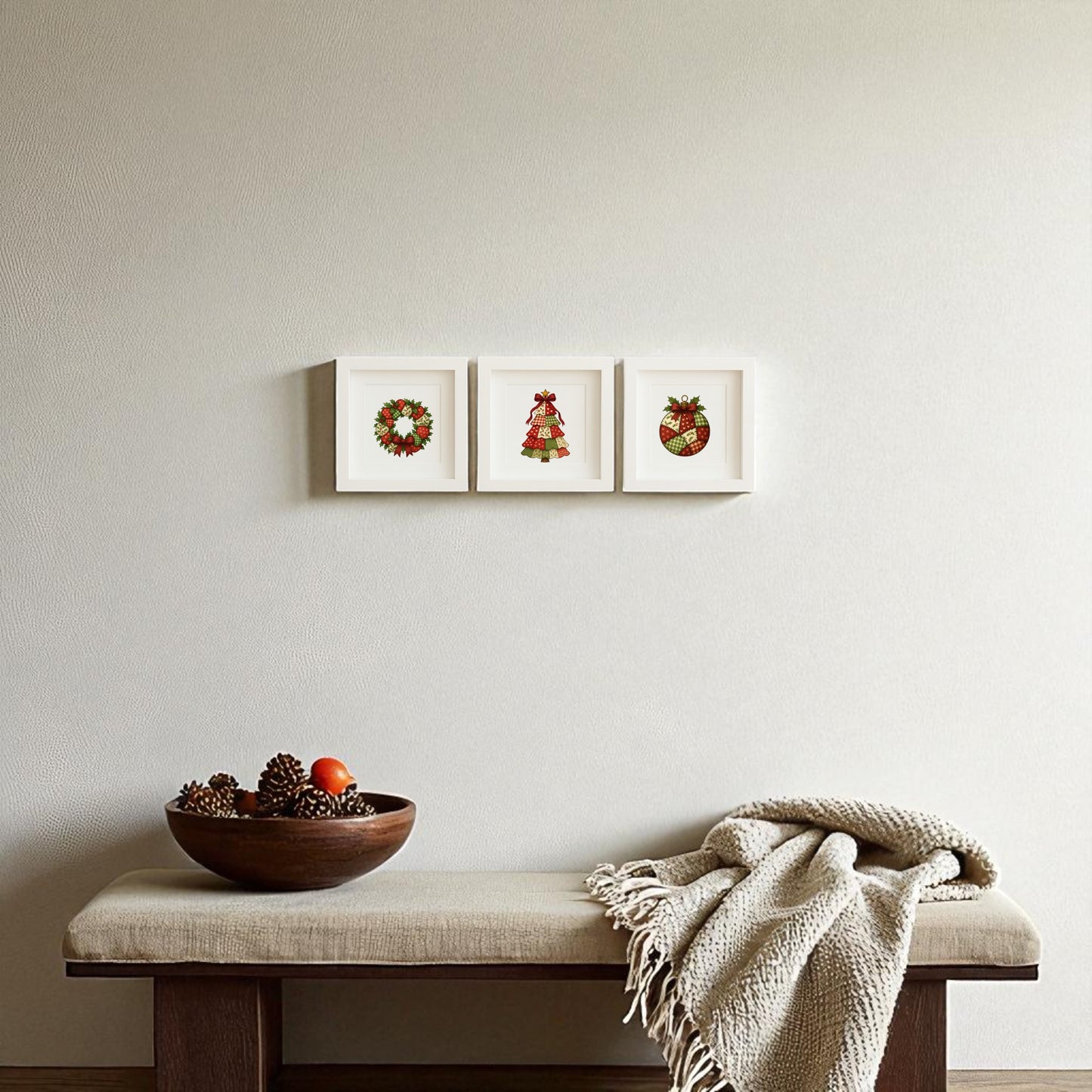 A minimalist room features a cushioned bench, beige blanket, and wooden bowl of pinecones. Above, the Mirabilia Boutique Patchwork Christmas Wall Art Trio—5x5 holiday shadowboxes—adds festive charm with wreath, tree, and stocking prints.