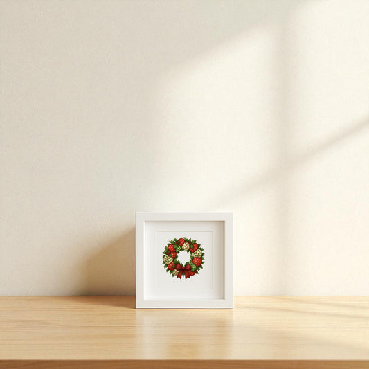 The Patchwork Christmas Wreath Sign | 5x5 Holiday Shadowbox Art by Mirabilia Boutique is displayed on a light wooden surface against a cream wall, sunlight casting soft shadows—a charming piece of farmhouse holiday decor.