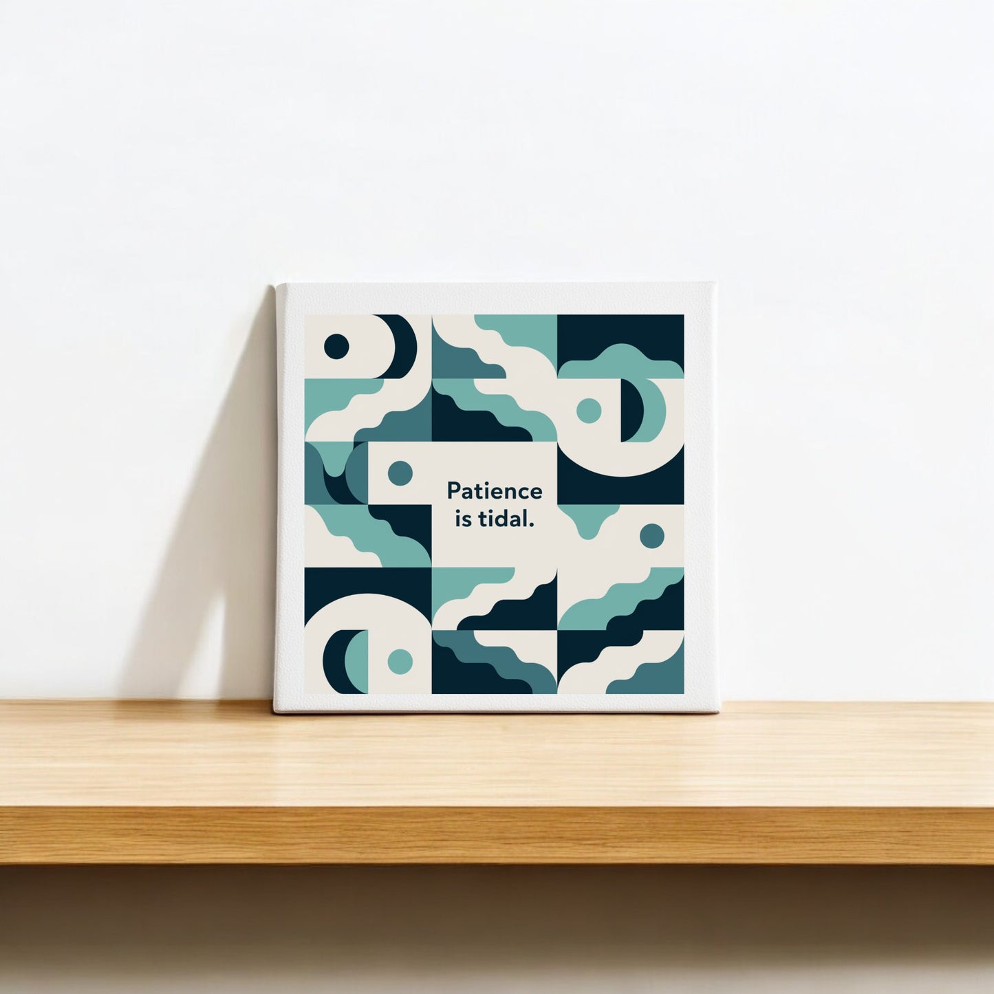 The Patience Is Tidal Canvas – Calm Coastal Wall Art by Mirabilia Boutique is a square piece with abstract blue and cream waves and the phrase "Patience is tidal." centered, perfect for display on a wooden shelf.