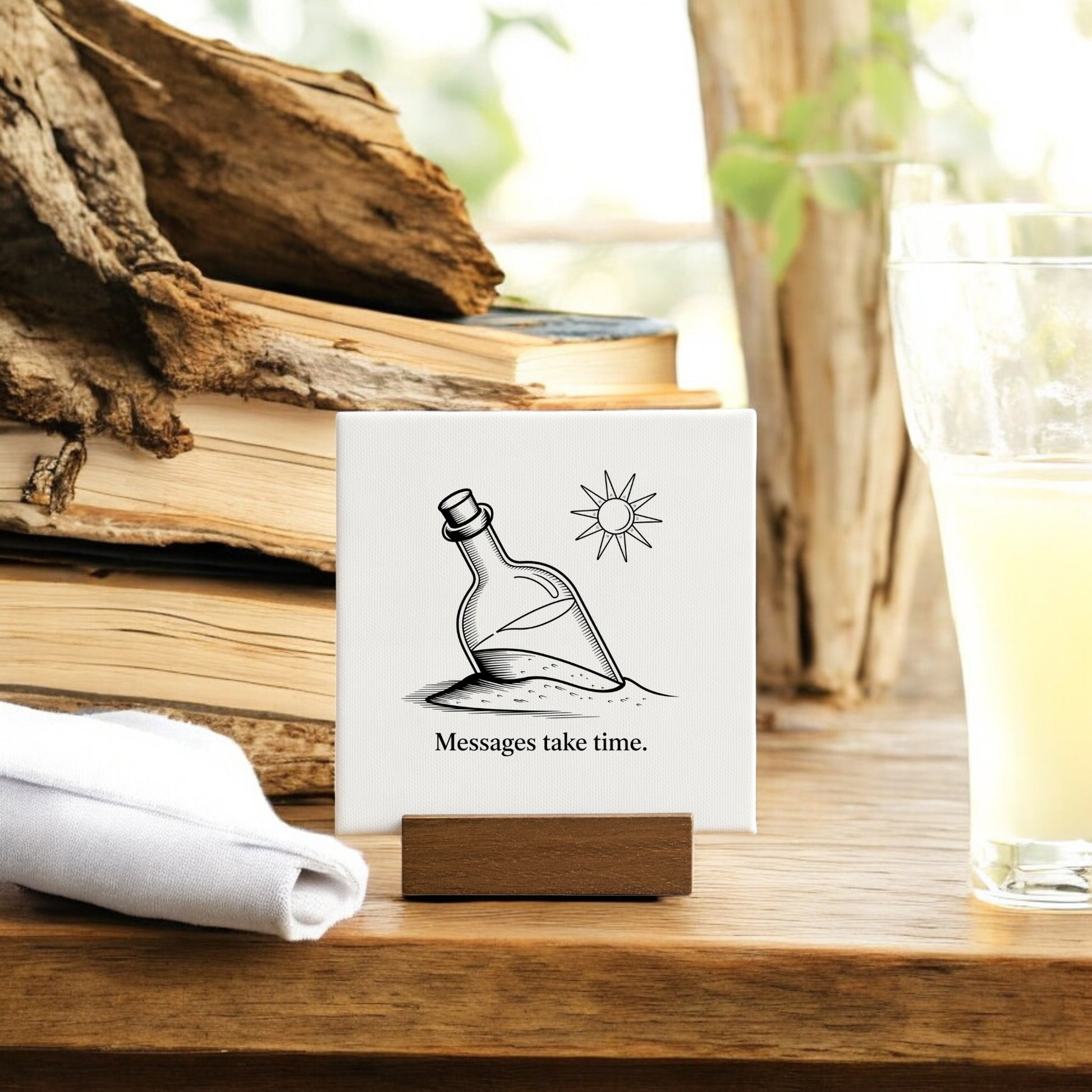 The Messages Take Time Mini Canvas – Desk Art with Wood Stand by Mirabilia Boutique features a "message in a bottle" design and serves as inspirational desk decor, perfect next to books and a refreshing glass of lemonade.