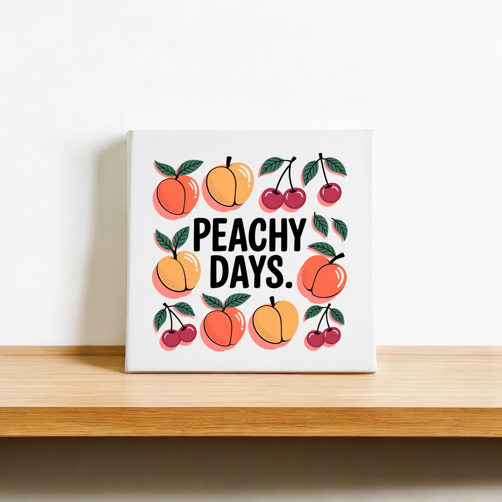 The Peachy Days Canvas from Mirabilia Boutique features bold "PEACHY DAYS." text, surrounded by peaches and cherries, on a white background. This cheerful fruit-inspired wall art adds a fresh summer vibe to your home decor.