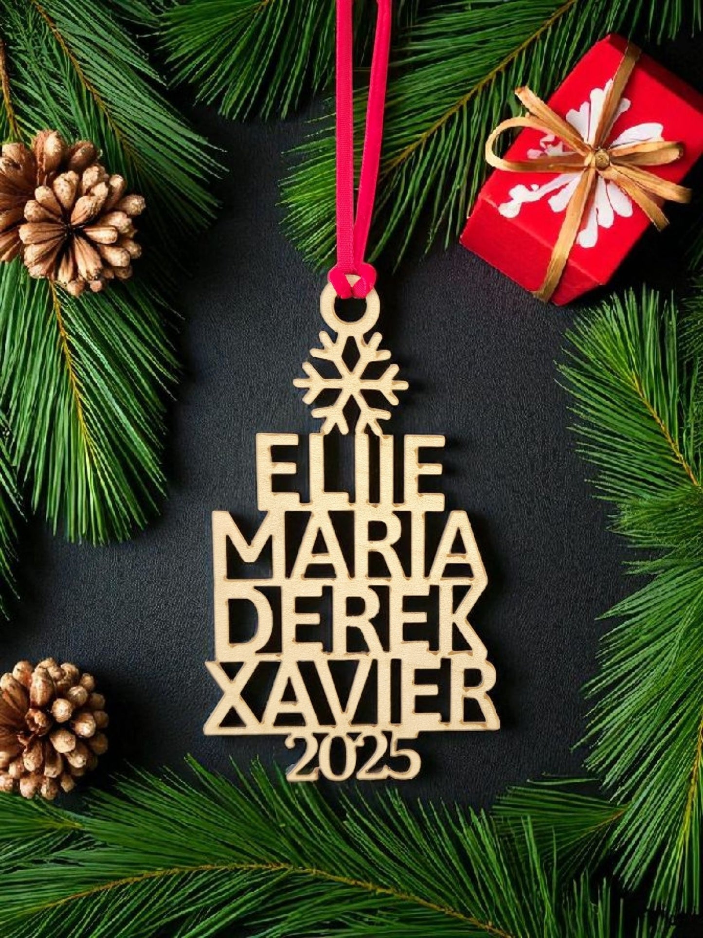 The Custom Family Christmas Ornament With Year by Mirabilia Boutique features names (Ellie, Maria, Derek, Xavier) and "2025," hanging on a red ribbon. This personalized holiday decor is a perfect family keepsake for your tree.