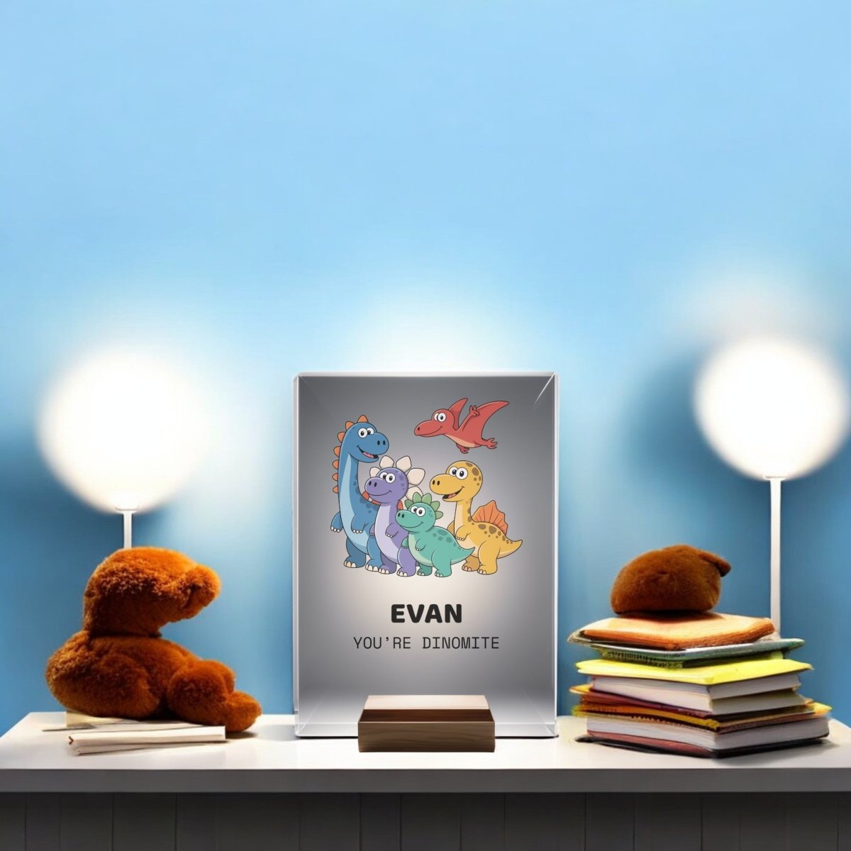 A children’s room shelf features two teddy bears, a stack of books, and a “Personalized Dinosaur Night Light for Kids” by Mirabilia Boutique glowing softly, alongside framed art with "Evan" and "You’re dinomite.