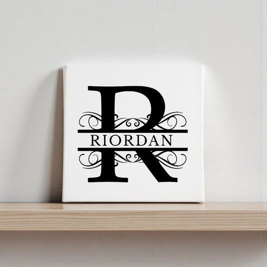 The Mirabilia Boutique Custom Monogram Canvas with Family Name – 8x8 showcases a bold black "R" with ornate swirls and "RIORDAN" across the center, creating elegant, personalized wall art for your home.