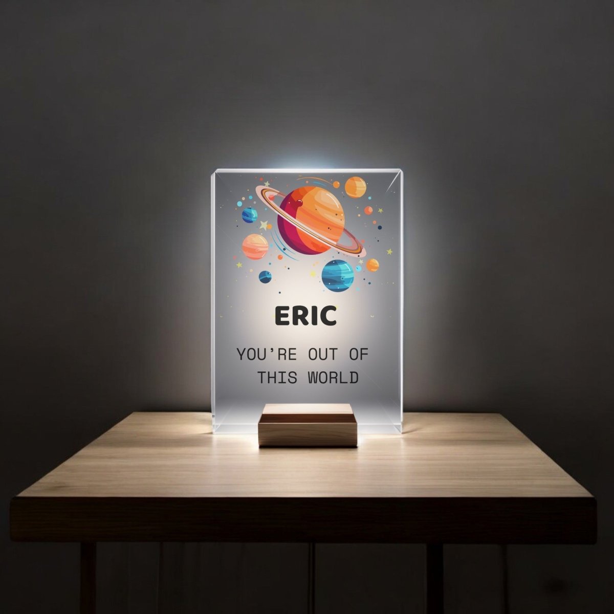 The Mirabilia Boutique Personalized Space Night Light for Kids features a glowing acrylic plaque with colorful cartoon planets and the message "ERIC YOU'RE OUT OF THIS WORLD," perfect for any space themed bedroom.