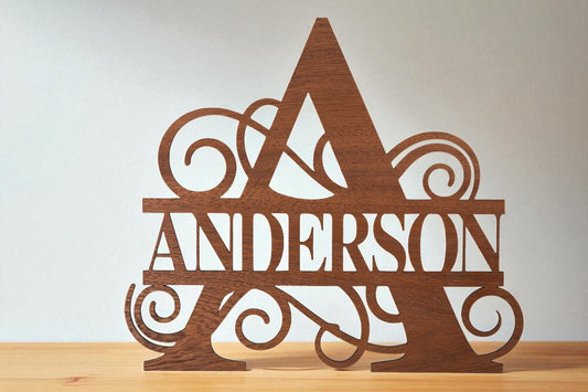 The Custom Walnut Name Cutout by Mirabilia Boutique is a handcrafted sign featuring an ornate "A" with "ANDERSON" cut across the middle, displayed on a wooden surface against a plain background. Perfect as personalized decor or a unique gift.