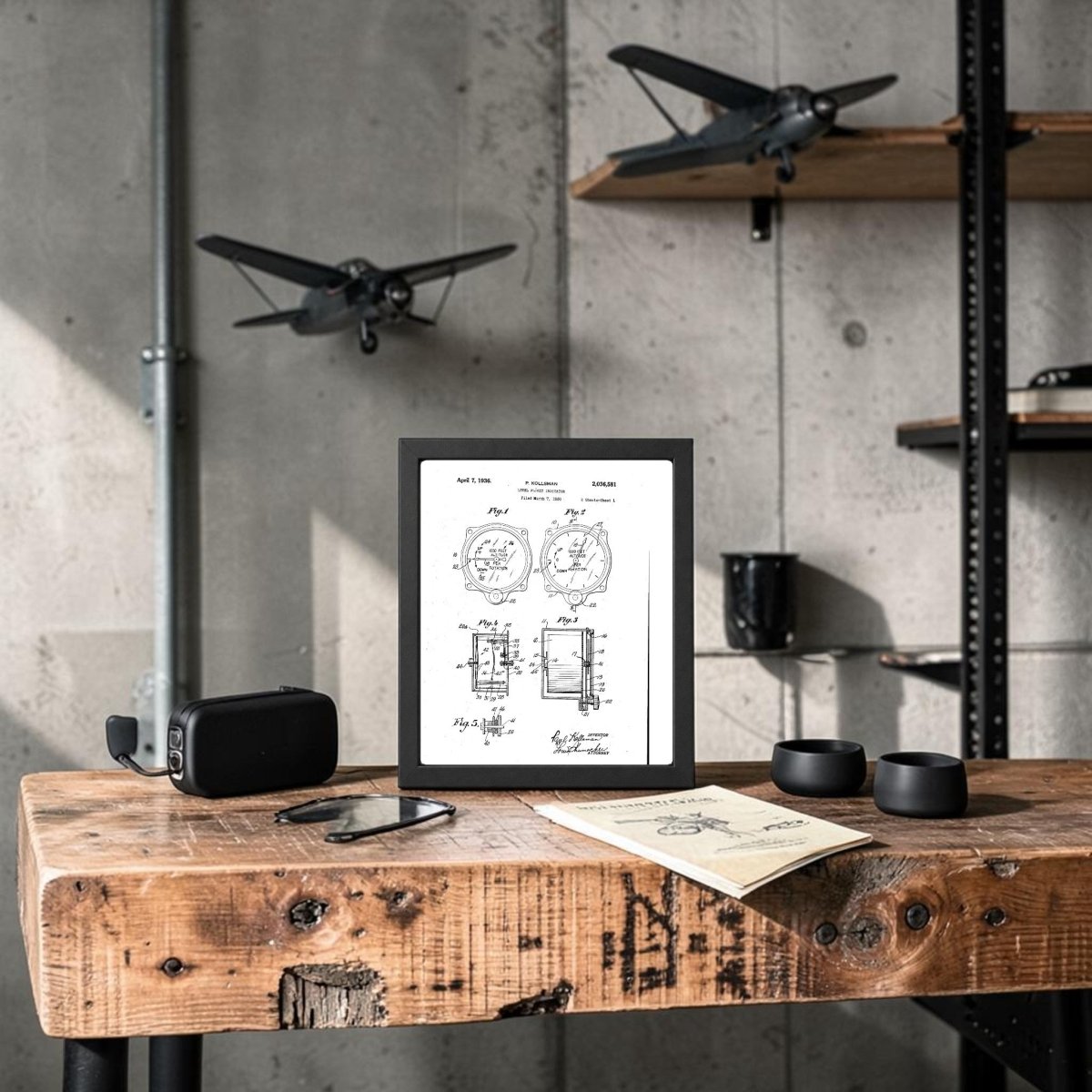 The Level Flight Indicator Patent Art Print by Mirabilia Boutique is framed and displayed on a rustic wooden desk with glasses, papers, and gadgets. Model airplanes and decor shelves hang on the concrete wall of this industrial aviation-themed room.