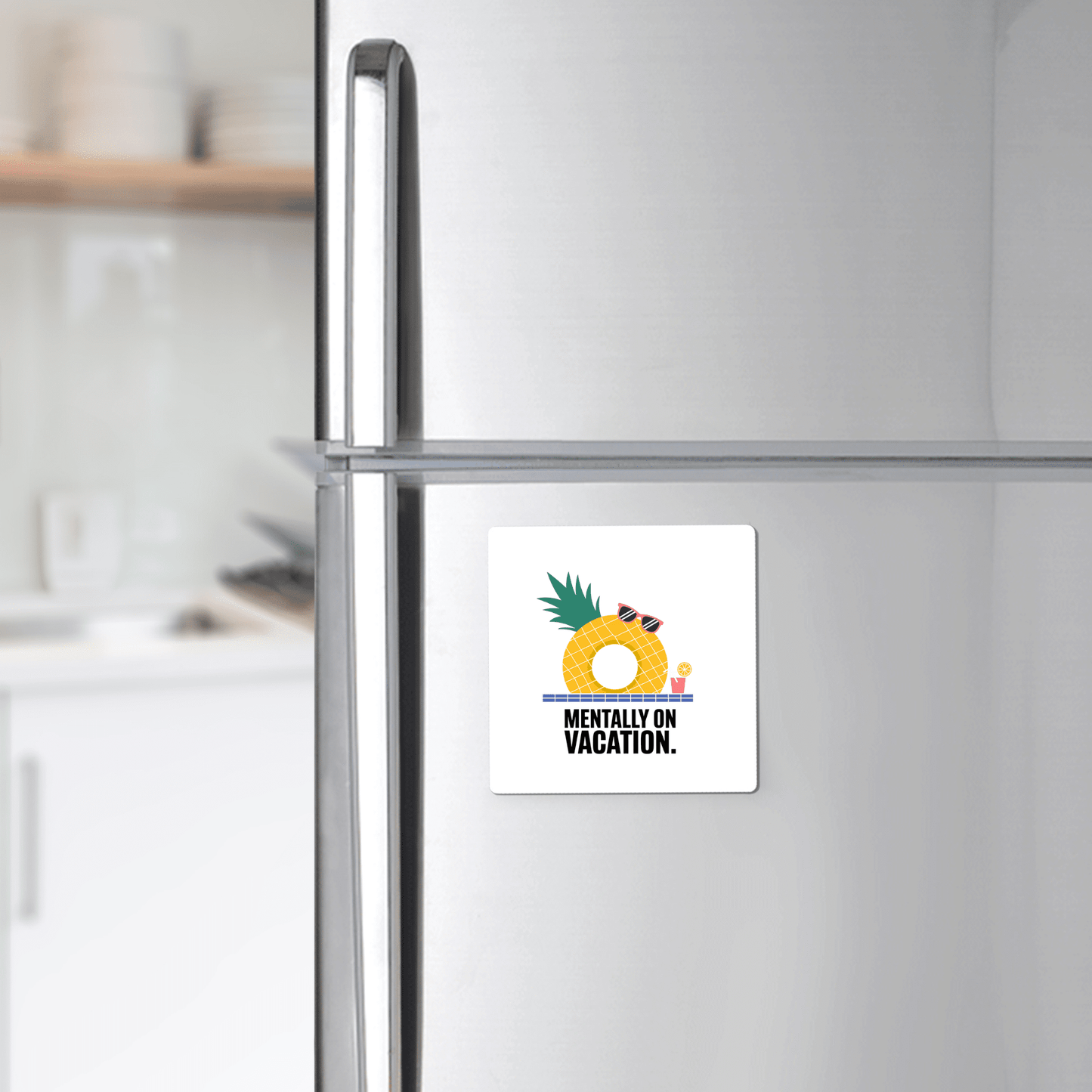 A silver fridge displays Mirabilia Boutique’s "Mentally on Vacation Magnet – Tropical Summer Vibes" with a pineapple, drink, and sunglasses above the phrase. Kitchen shelves with plates appear in the background.