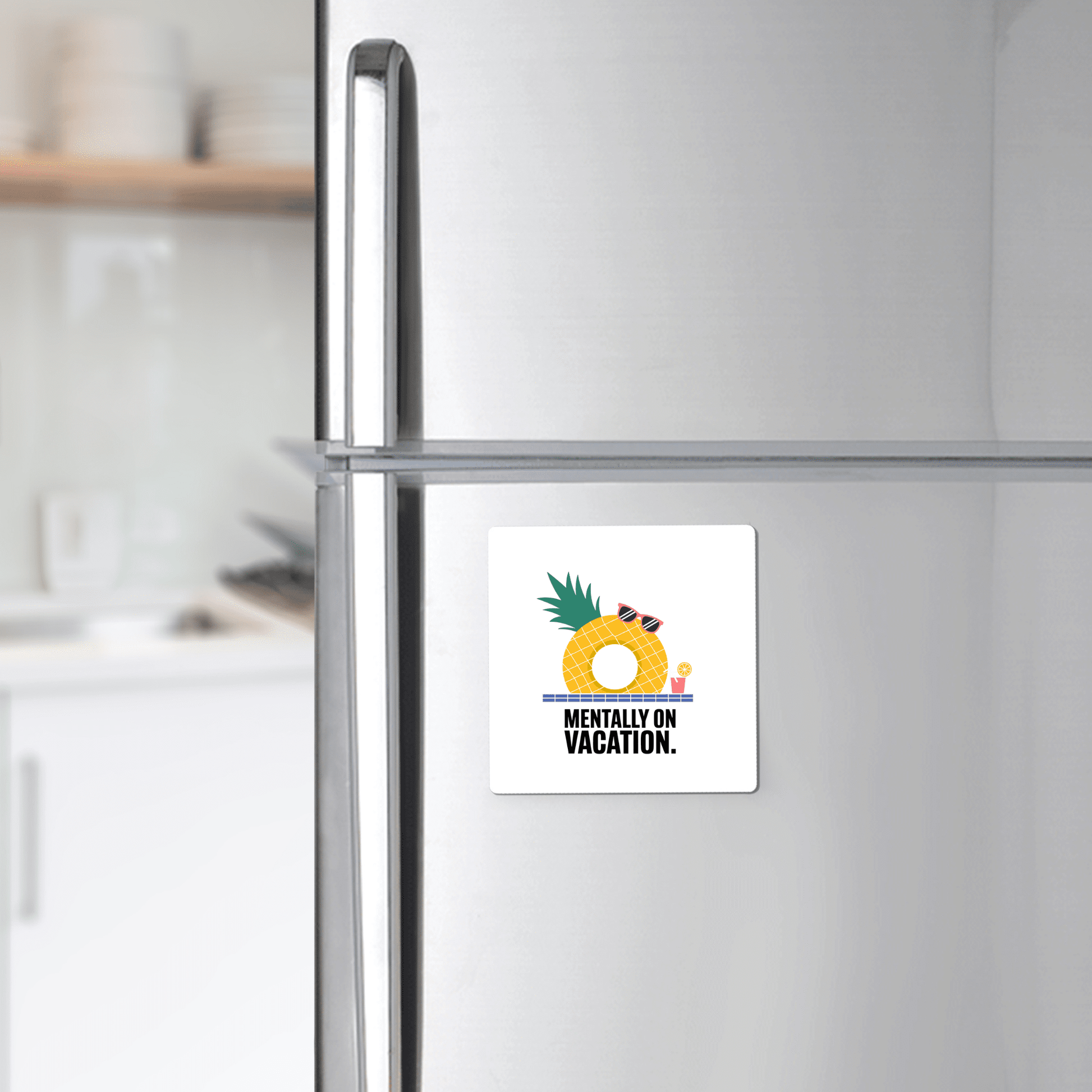 A silver fridge displays Mirabilia Boutique’s "Mentally on Vacation Magnet – Tropical Summer Vibes" with a pineapple, drink, and sunglasses above the phrase. Kitchen shelves with plates appear in the background.