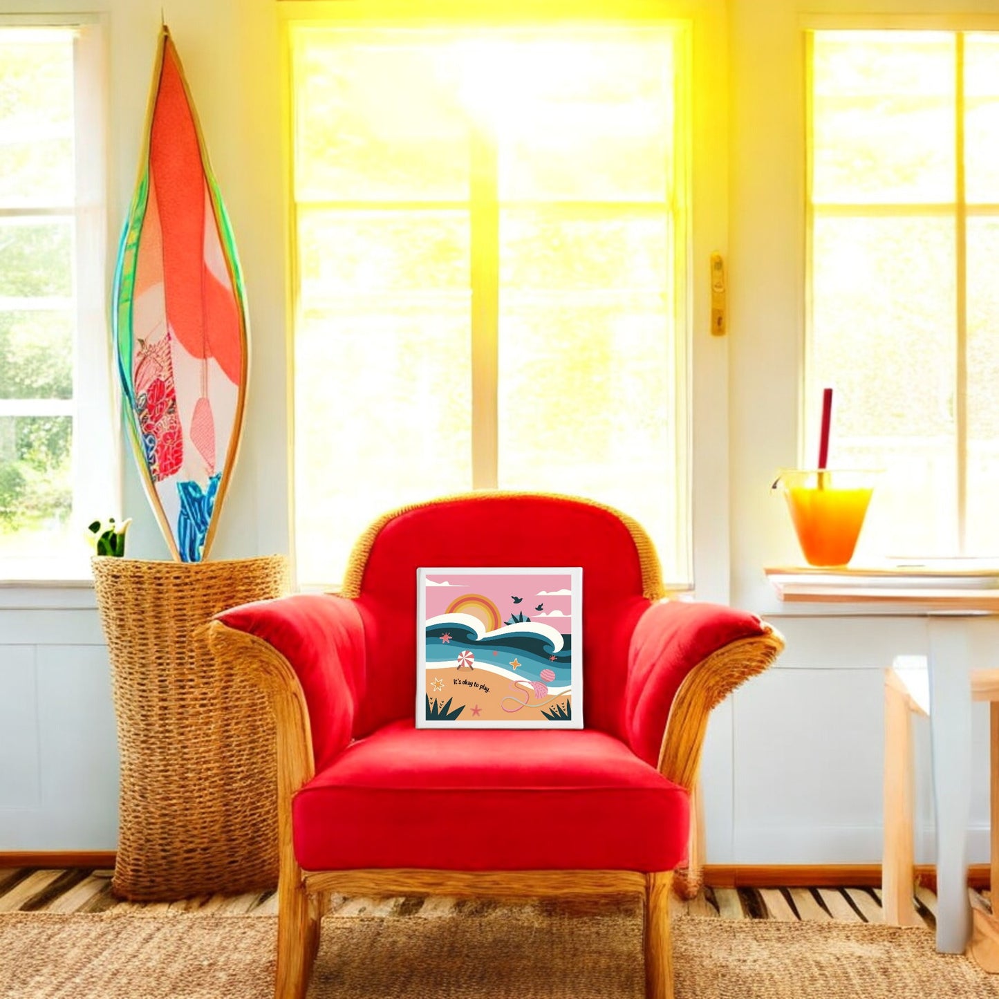 A wicker chair with a bright red cushion sits in the sunlit room. The It’s Okay to Play Canvas – Whimsical Beach Wall Art by Mirabilia Boutique rests on the chair, adding a vibrant beachy touch to the colorful home decor.