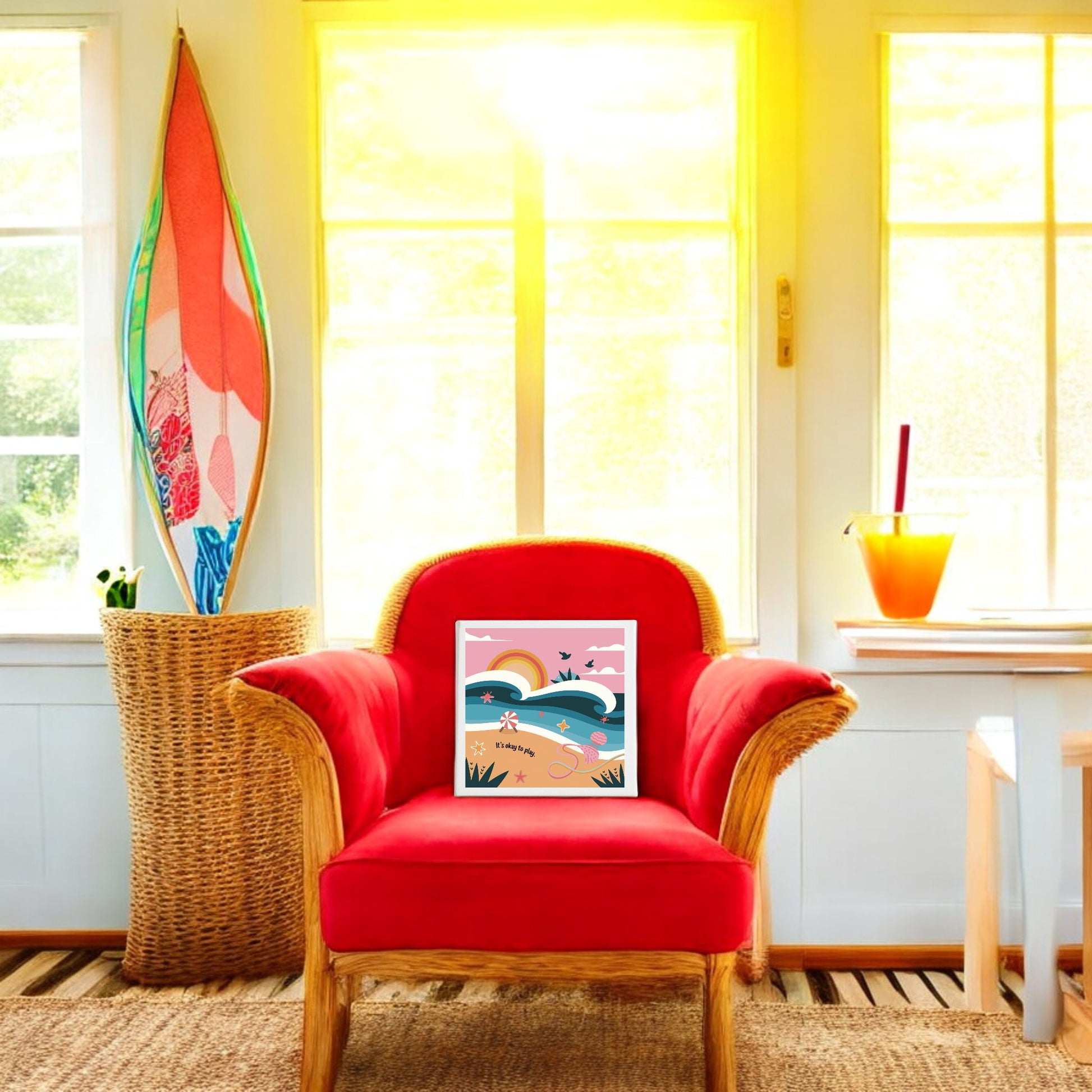 A wicker chair with a bright red cushion sits in the sunlit room. The It’s Okay to Play Canvas – Whimsical Beach Wall Art by Mirabilia Boutique rests on the chair, adding a vibrant beachy touch to the colorful home decor.