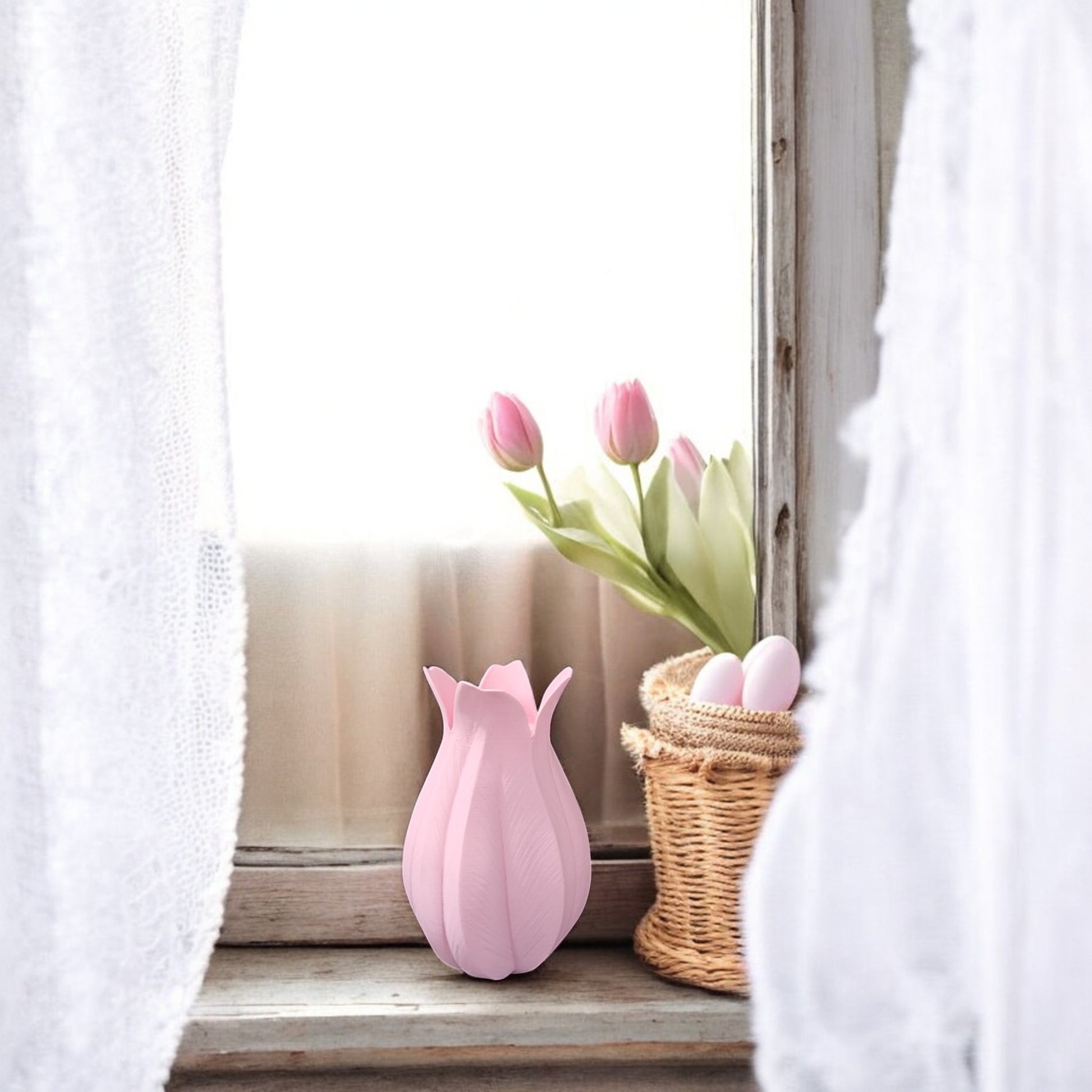 On a windowsill with sheer white curtains, a wicker basket of pink eggs and the Mirabilia Boutique Pink Tulip Vase – Decorative Accent for Easter & Mother’s Day create a cozy, soft-lit Easter display.