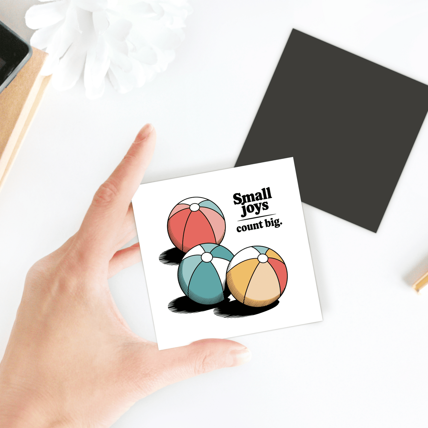 A hand holds the "Small Joys Count Big Magnet – Retro Summer Fridge Art" by Mirabilia Boutique, featuring three colorful beach balls and playful text—perfect retro decor for your fridge or a cheerful summer magnet display.