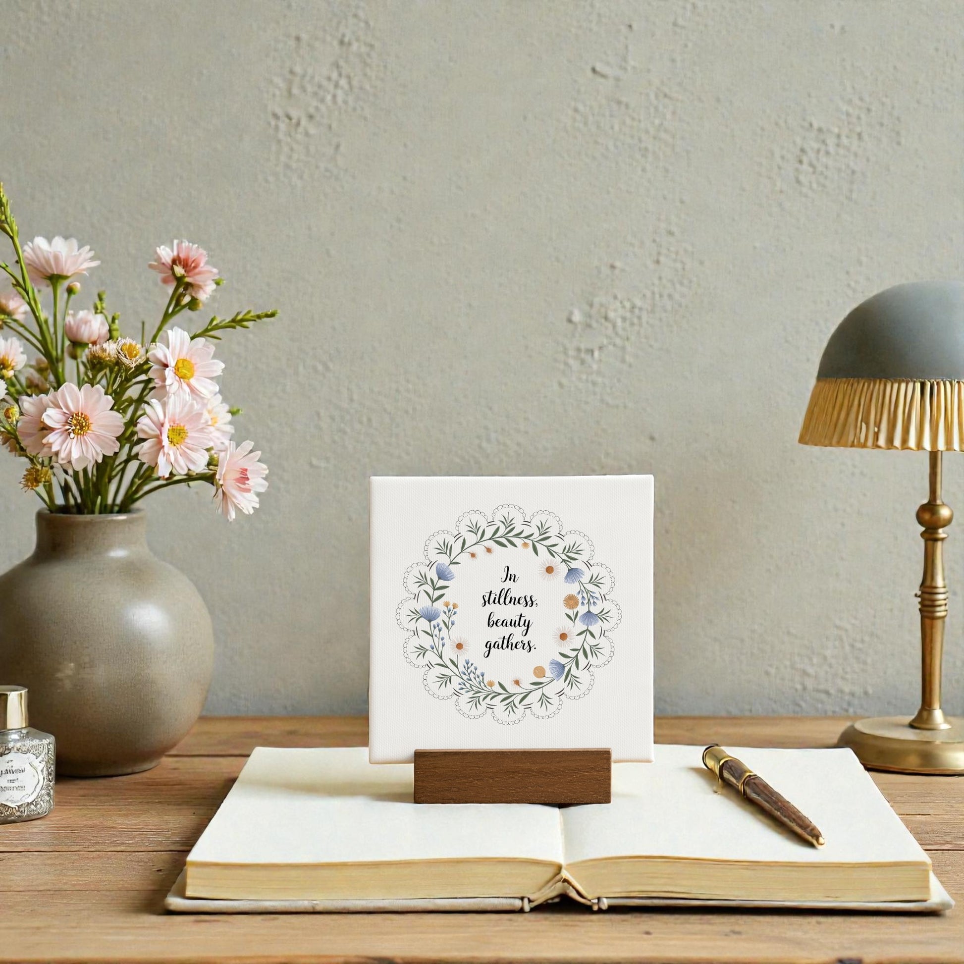 The Mirabilia Boutique "In Stillness Beauty Gathers" Mini Canvas Sign features a floral design and wooden holder, bringing handcrafted charm to your meditation shelf decor or book nook.