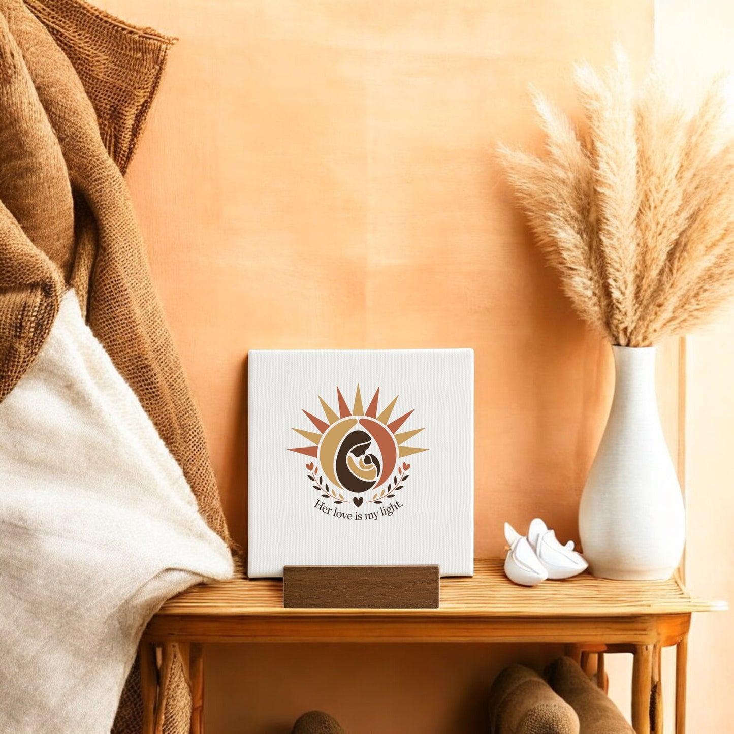 The Her Love Is My Light Mini Sign – Mother’s Day Canvas by Mirabilia Boutique features a sun and mother with child, captioned “Her love is my light”—a beautiful, warm-toned keepsake for moms, shown on a cozy table setting.