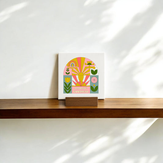 The Mirabilia Boutique "Radiate Goodness" Mini Canvas Sign with Base features colorful abstract flowers and rainbows, adding an encouraging touch to your shelf or desk in soft sunlight against a white wall.