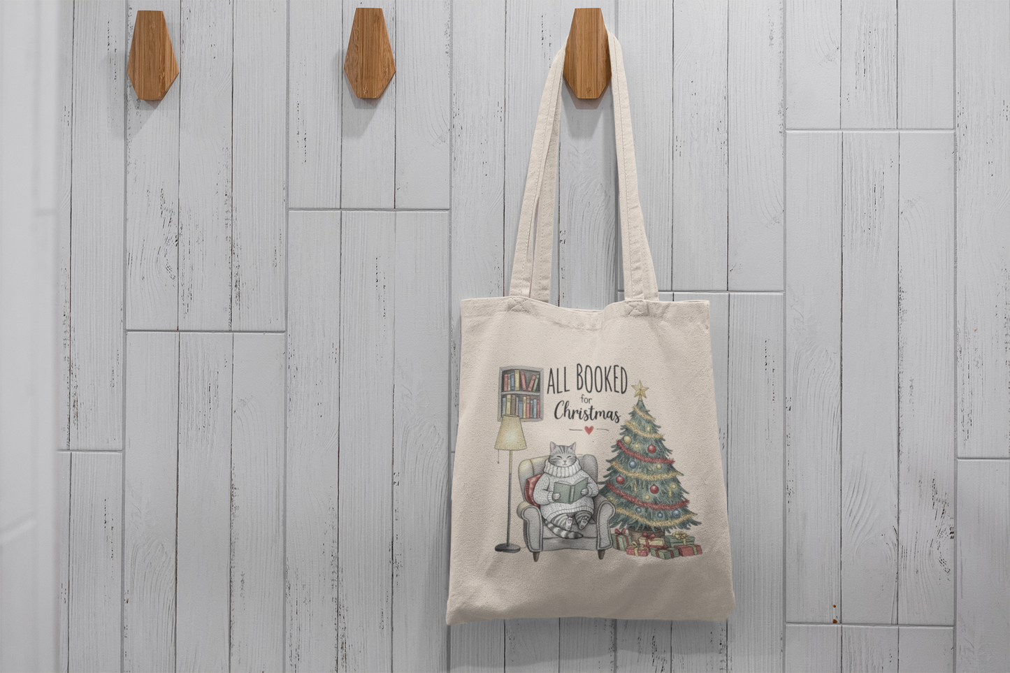 The Mirabilia Boutique “All Booked for Christmas Cat Tote Bag” is a beige tote featuring a cat reading by the tree—perfect as a cozy holiday accessory or gift for book lovers.